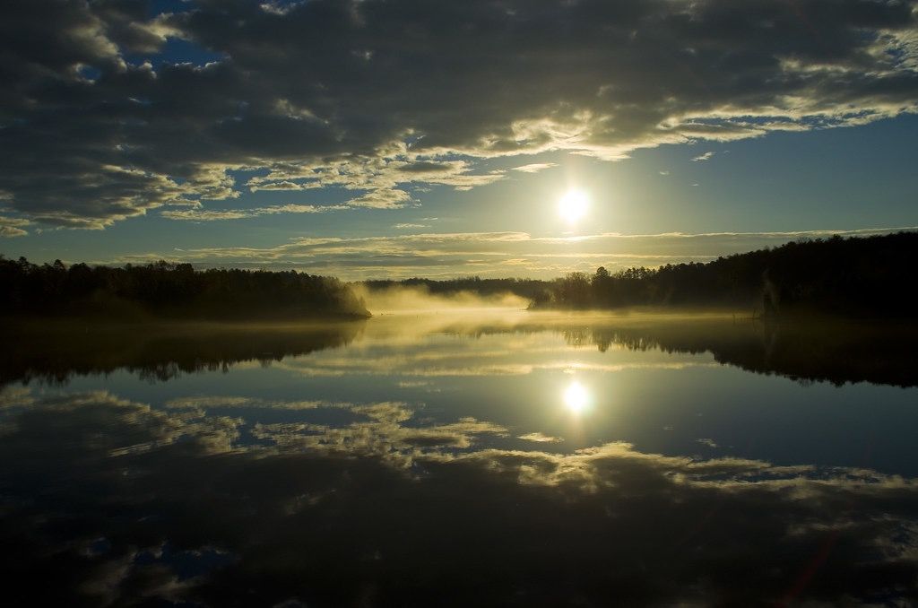 Golden sun reflects on a misty lake with dark trees and dramatic clouds. - Randleman Lake double loop