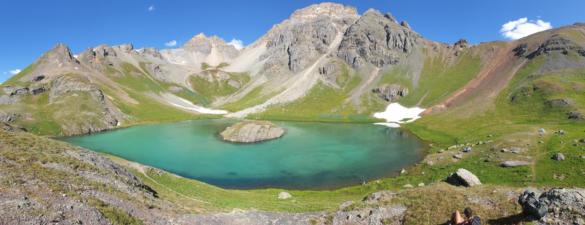 Panoramic view of a turquoise lake with a rocky island, surrounded by mountains.