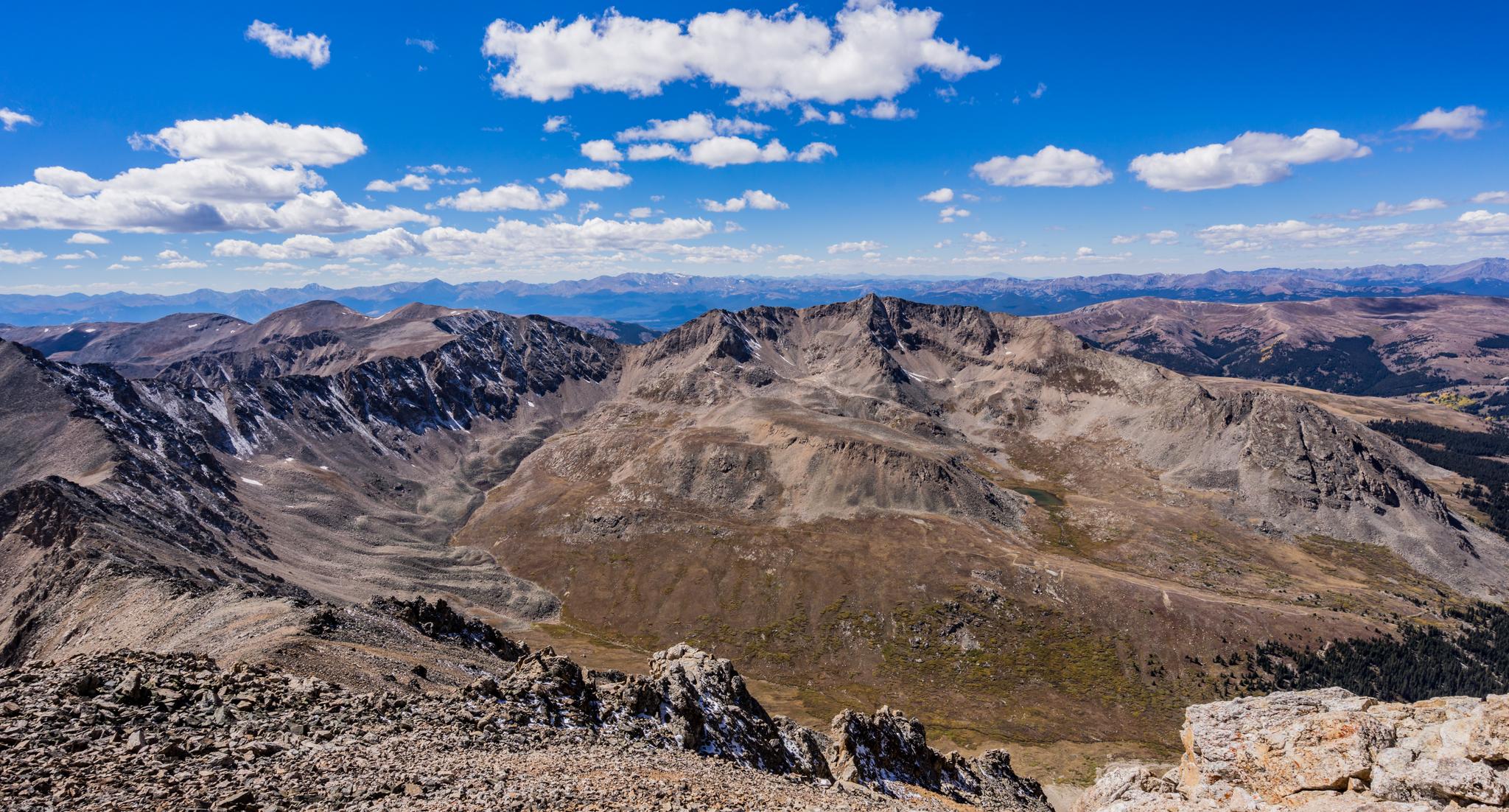 Expansive view of rugged, rocky mountains and valleys under a bright, cloudy sky.