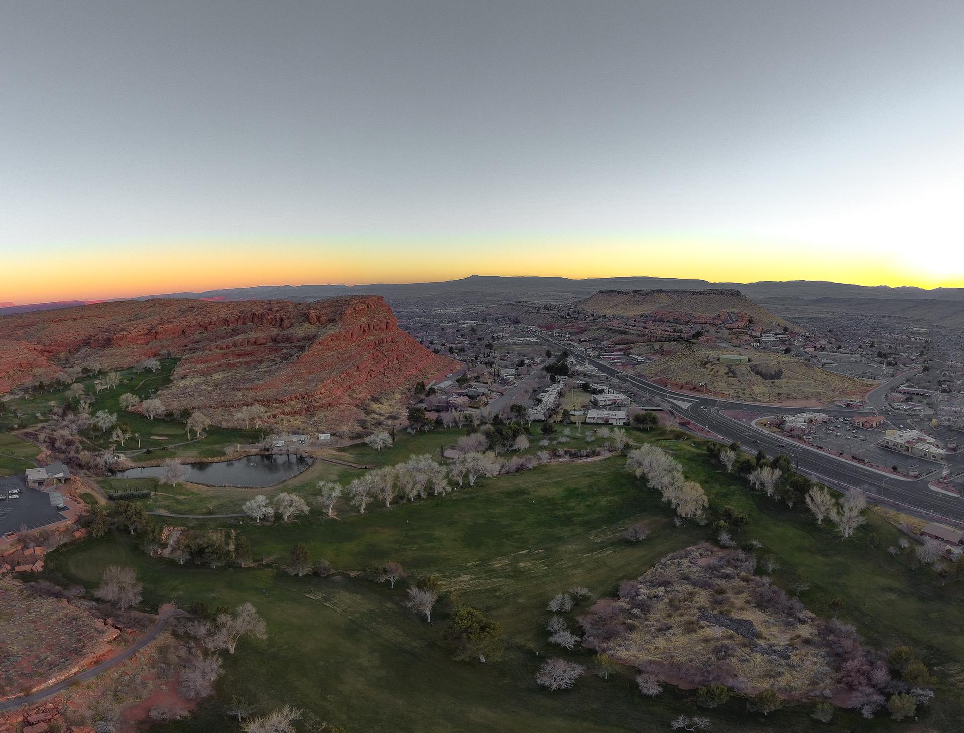 Panoramic view of a town, green fields, and red cliffs under a sunset sky.