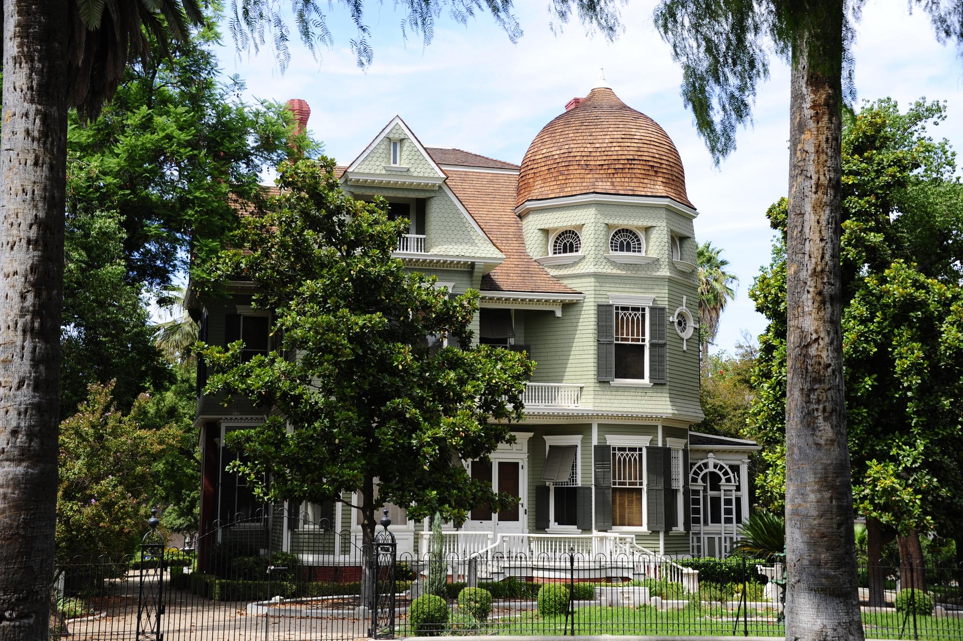Ornate house with a domed turret, surrounded by lush green trees in daylight.