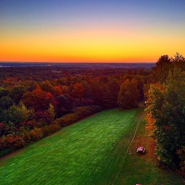 Aerial view of a vibrant sunset over a forest and green field.