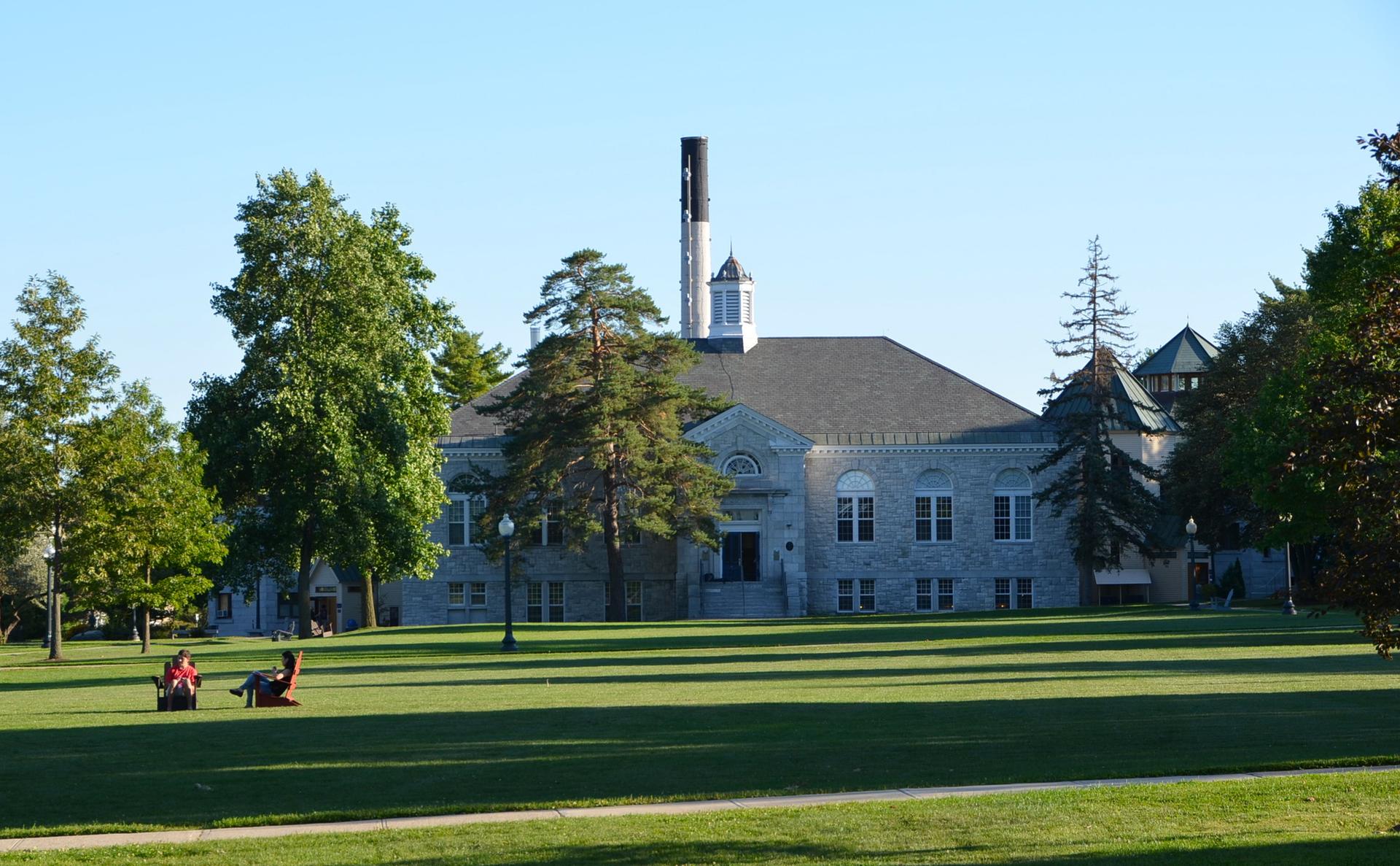 Large stone building behind a sunny green lawn with two people relaxing.