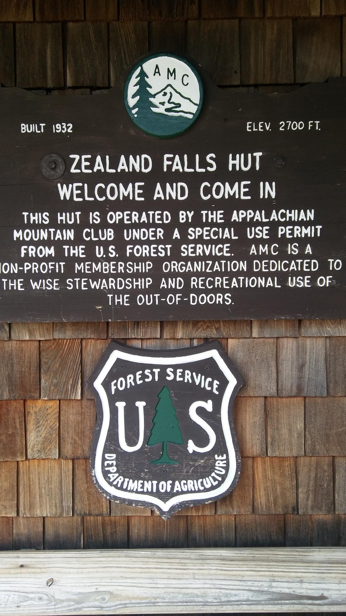 Informational sign on a wooden shingle wall with text and logos.