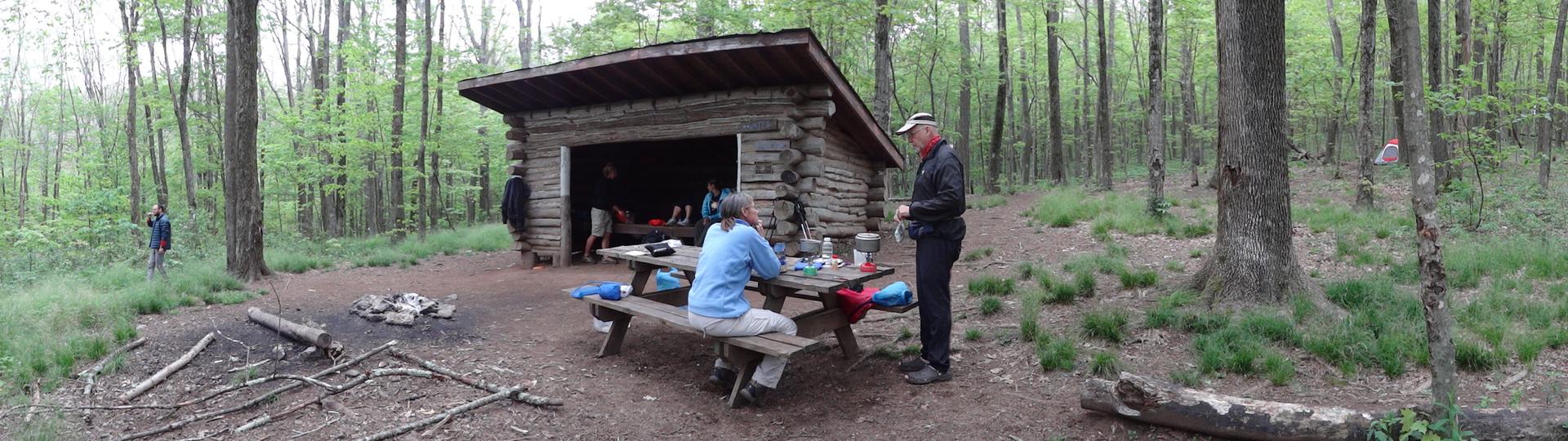 Hikers resting at a rustic wooden shelter in a green forest.