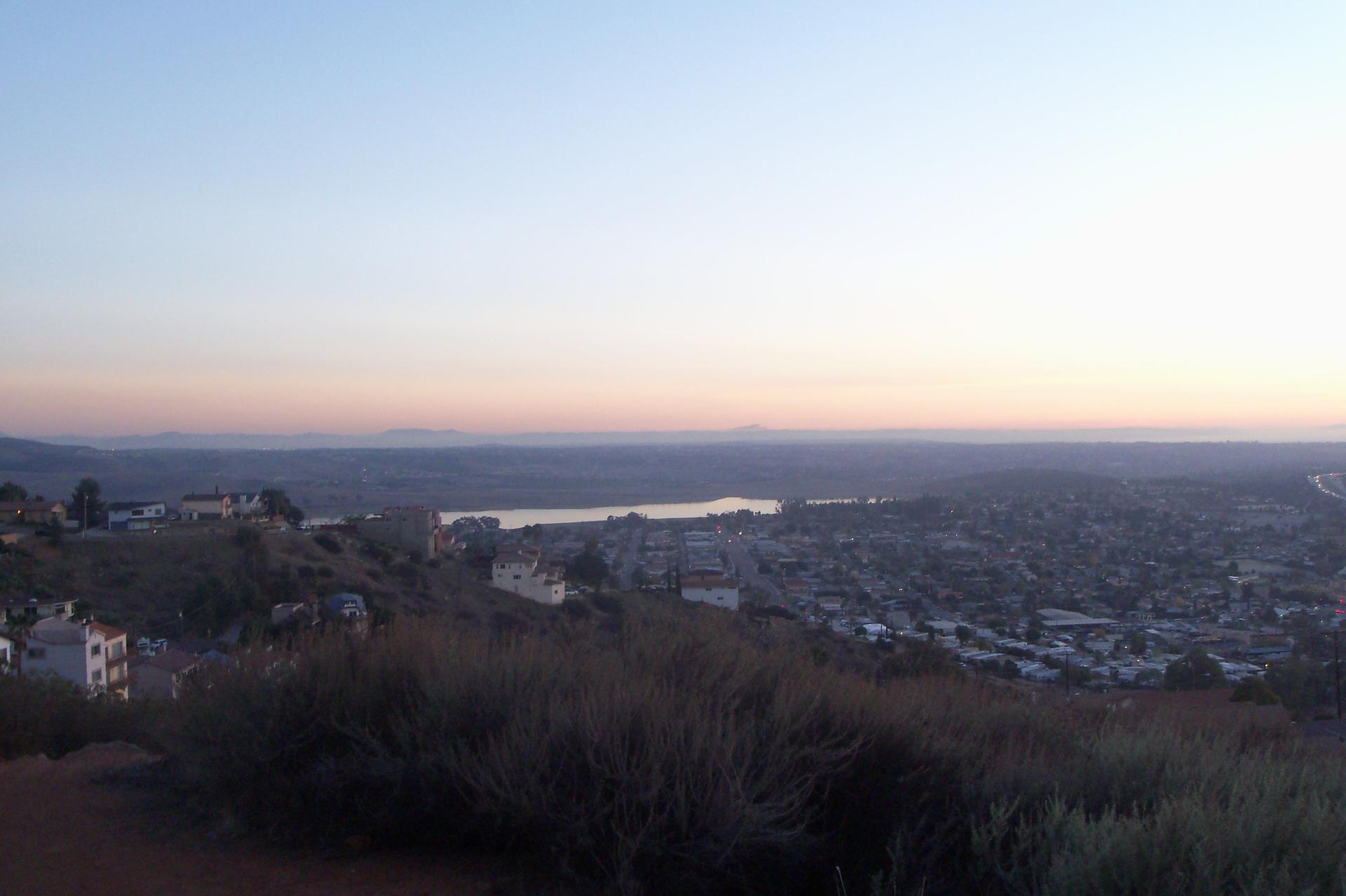 Expansive view of a town, lake, and hills under a serene, colorful twilight sky.