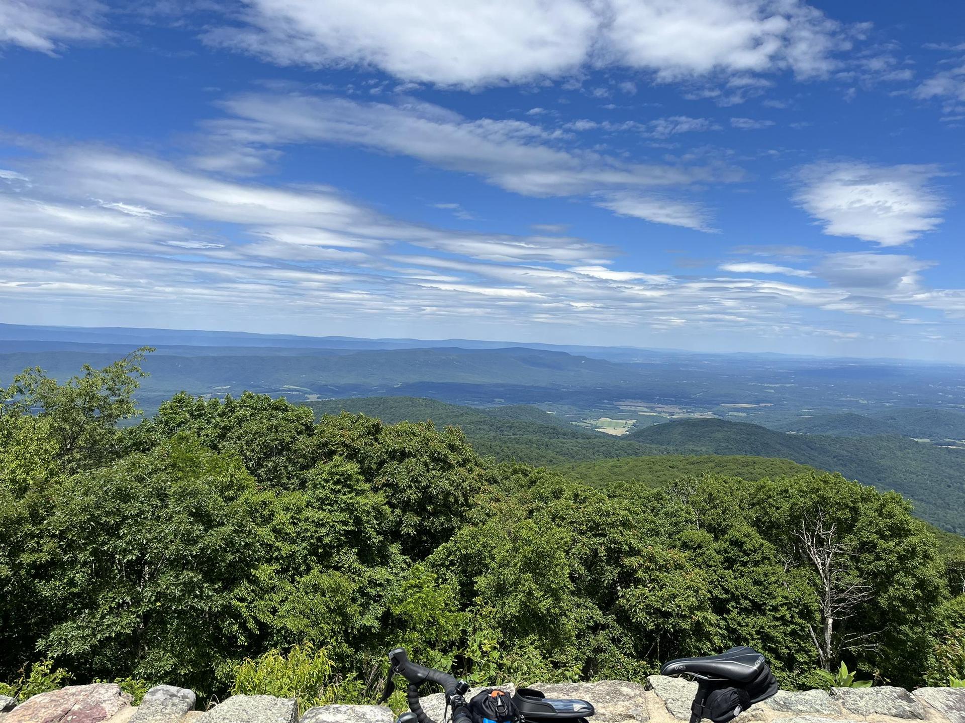 Sunny mountain vista with green trees and a bicycle on a stone wall.