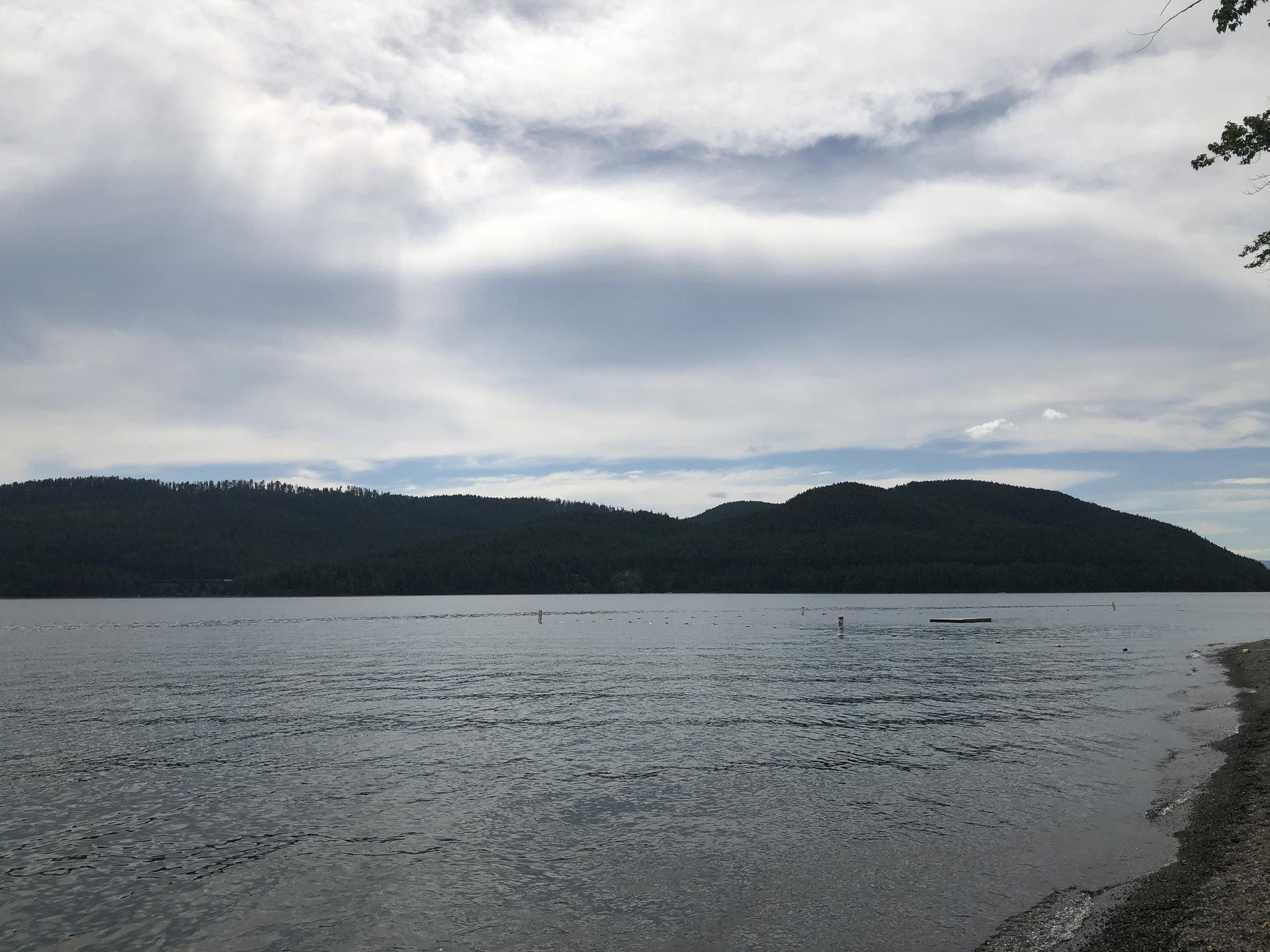 A wide lake with dark forested mountains under a cloudy sky.