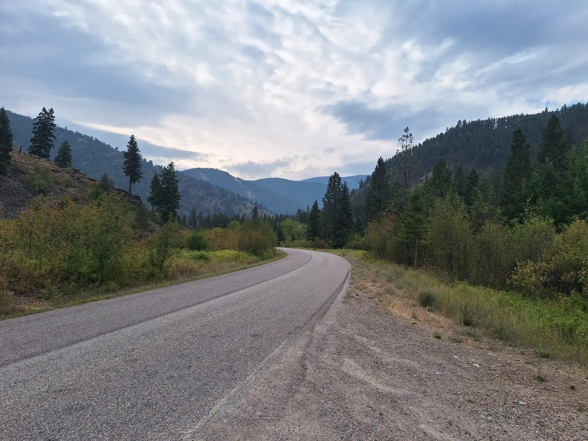 Paved road curves through a forested mountain valley under an overcast sky.