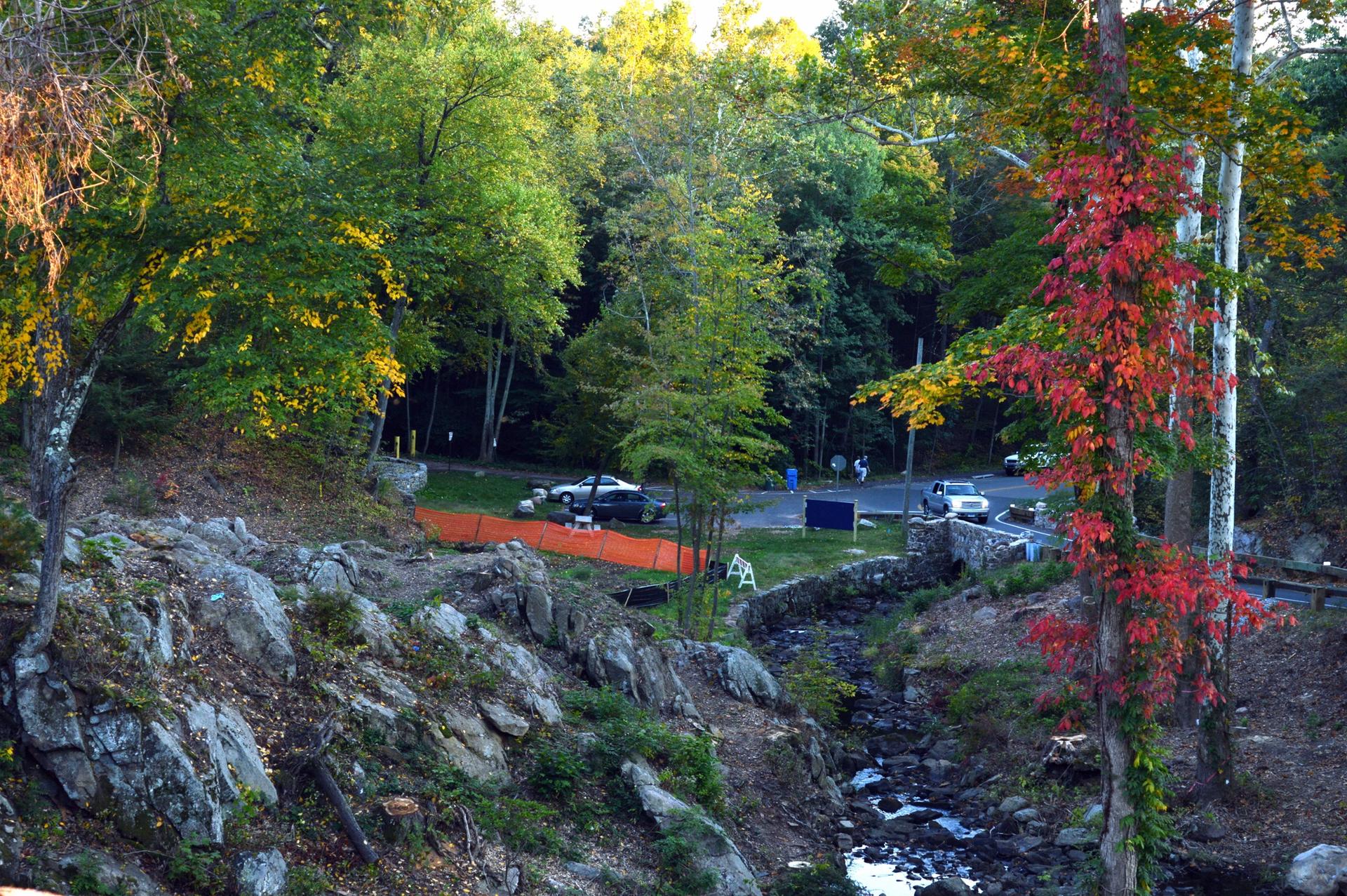 Stream flowing through a rocky landscape with colorful trees and parked cars.