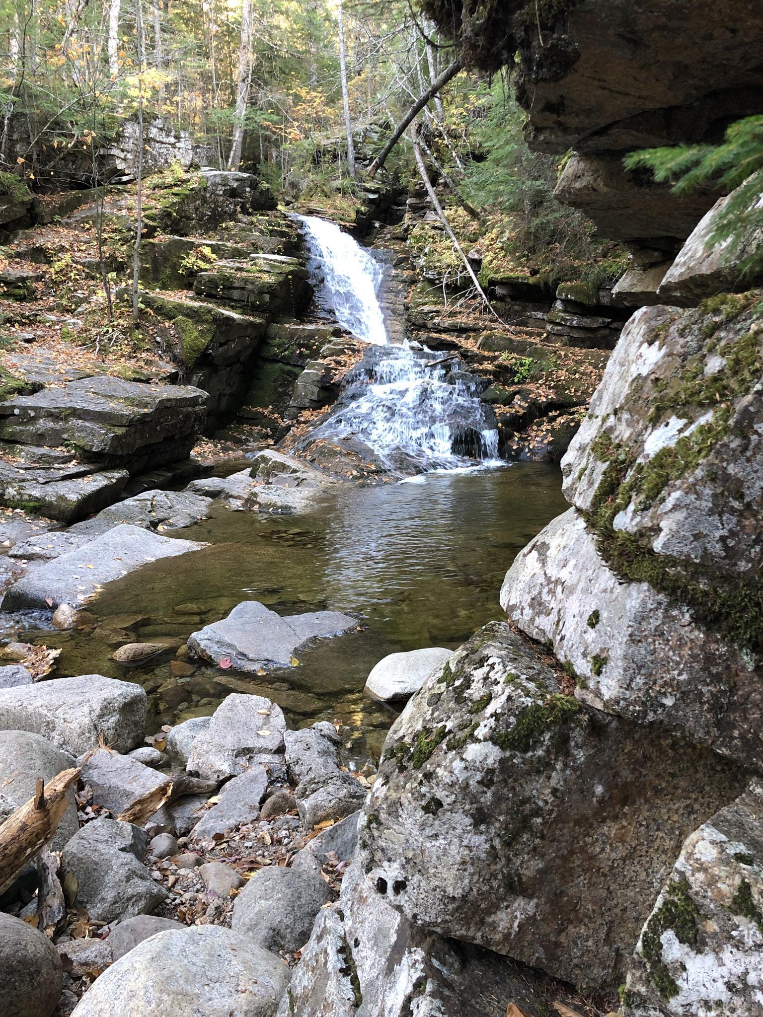 A beautiful waterfall cascades into a rocky pool surrounded by autumn forest.