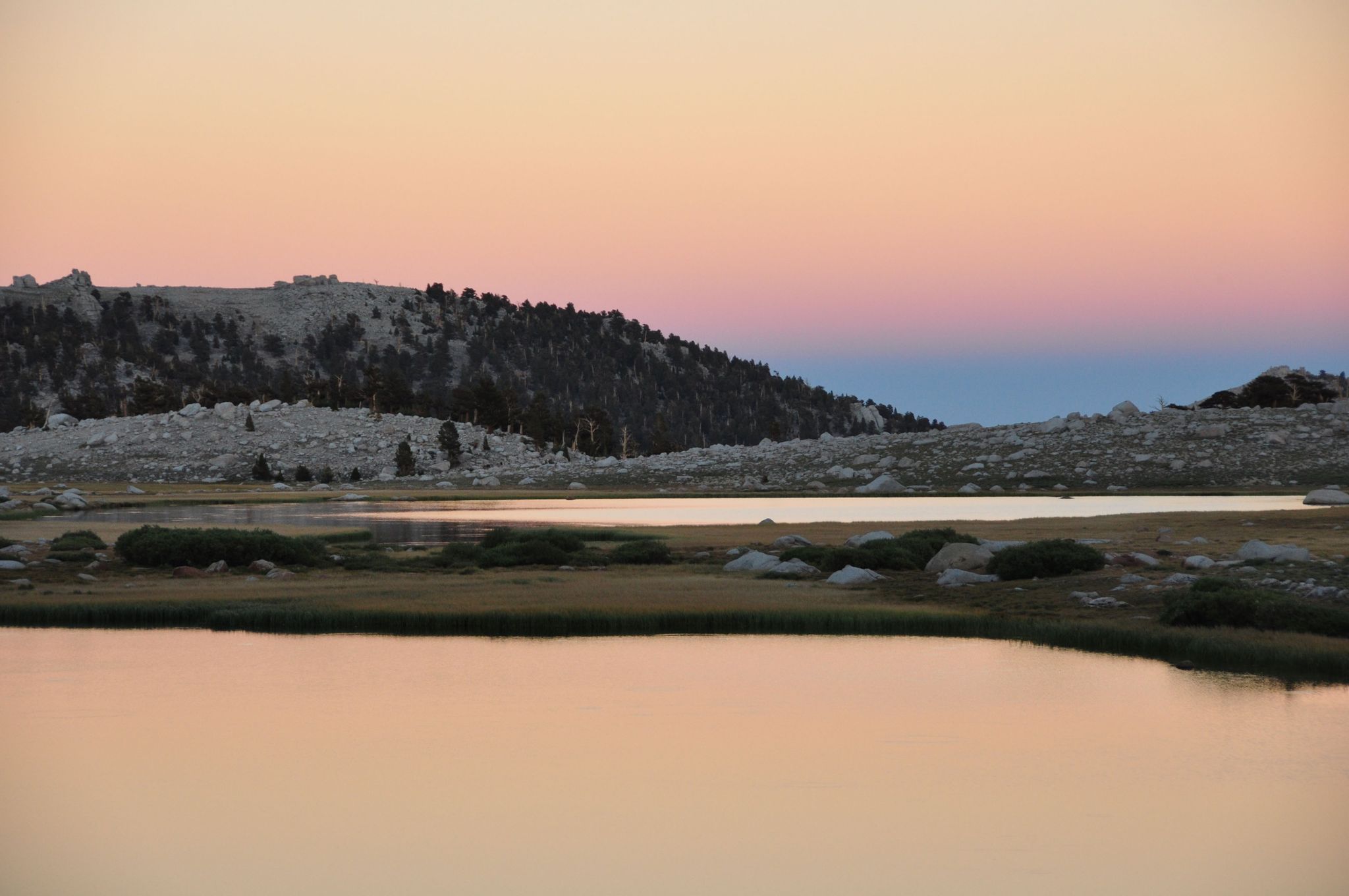 Calm lake reflecting a pastel sunset sky with distant hills and sparse trees. - Cottonwood Lakes and Army Pass Loop