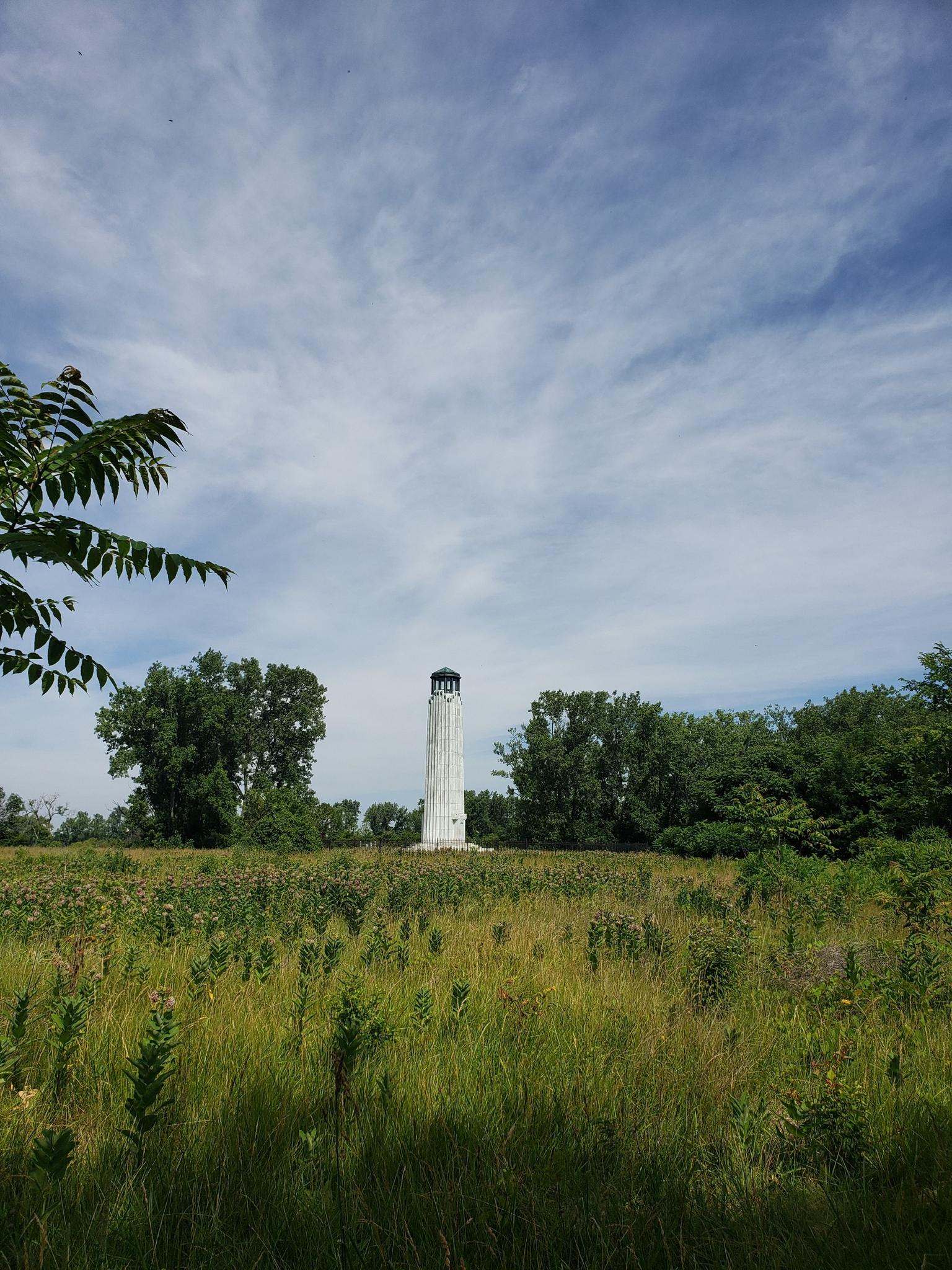 Tall white tower in a grassy field under a partly cloudy sky.
