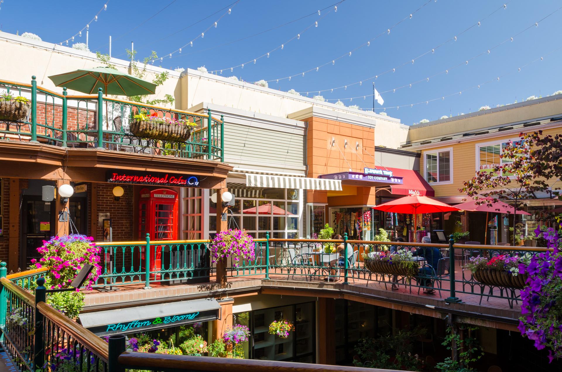 Multi-level outdoor shopping area with colorful flowers under bright sunlight.