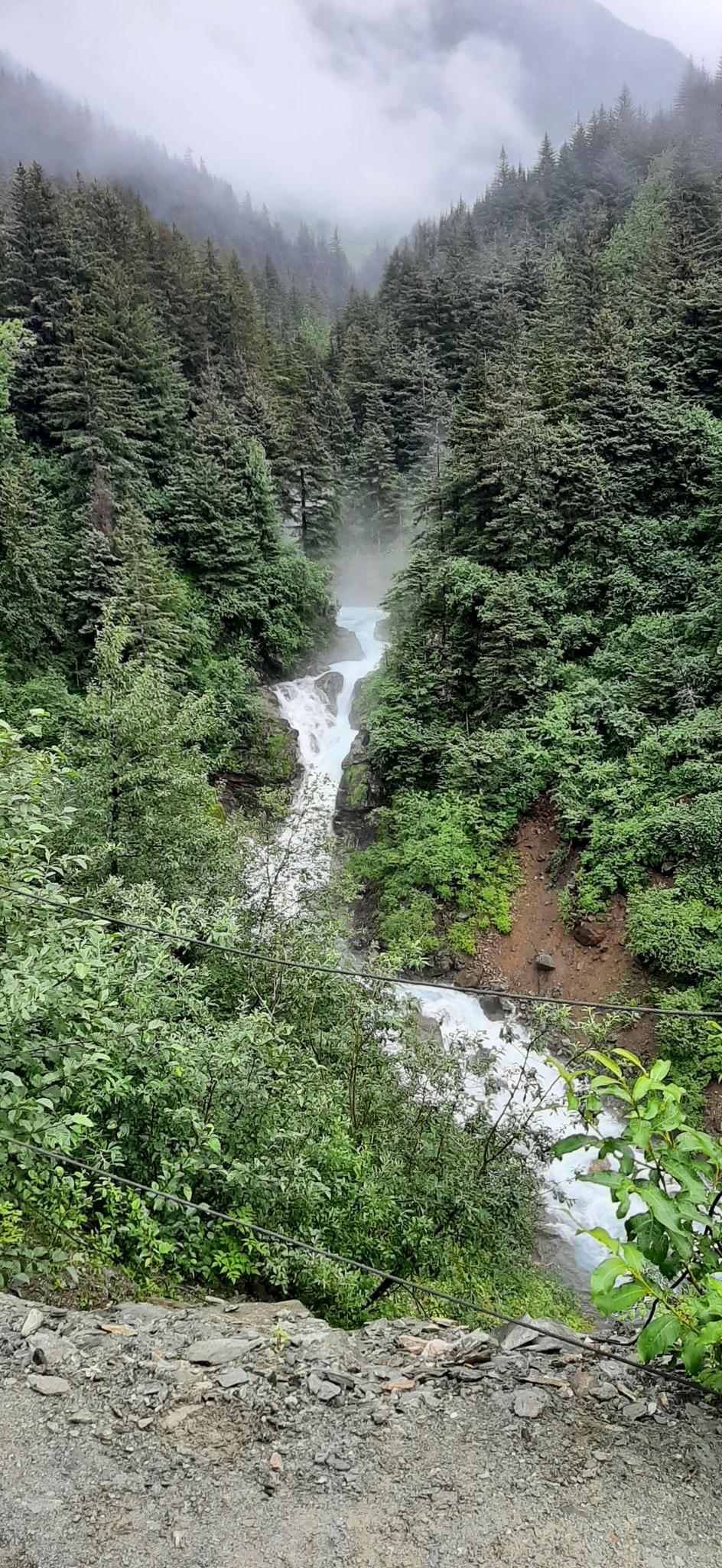 Waterfall cascades through a dense green forest with misty mountains in the background.