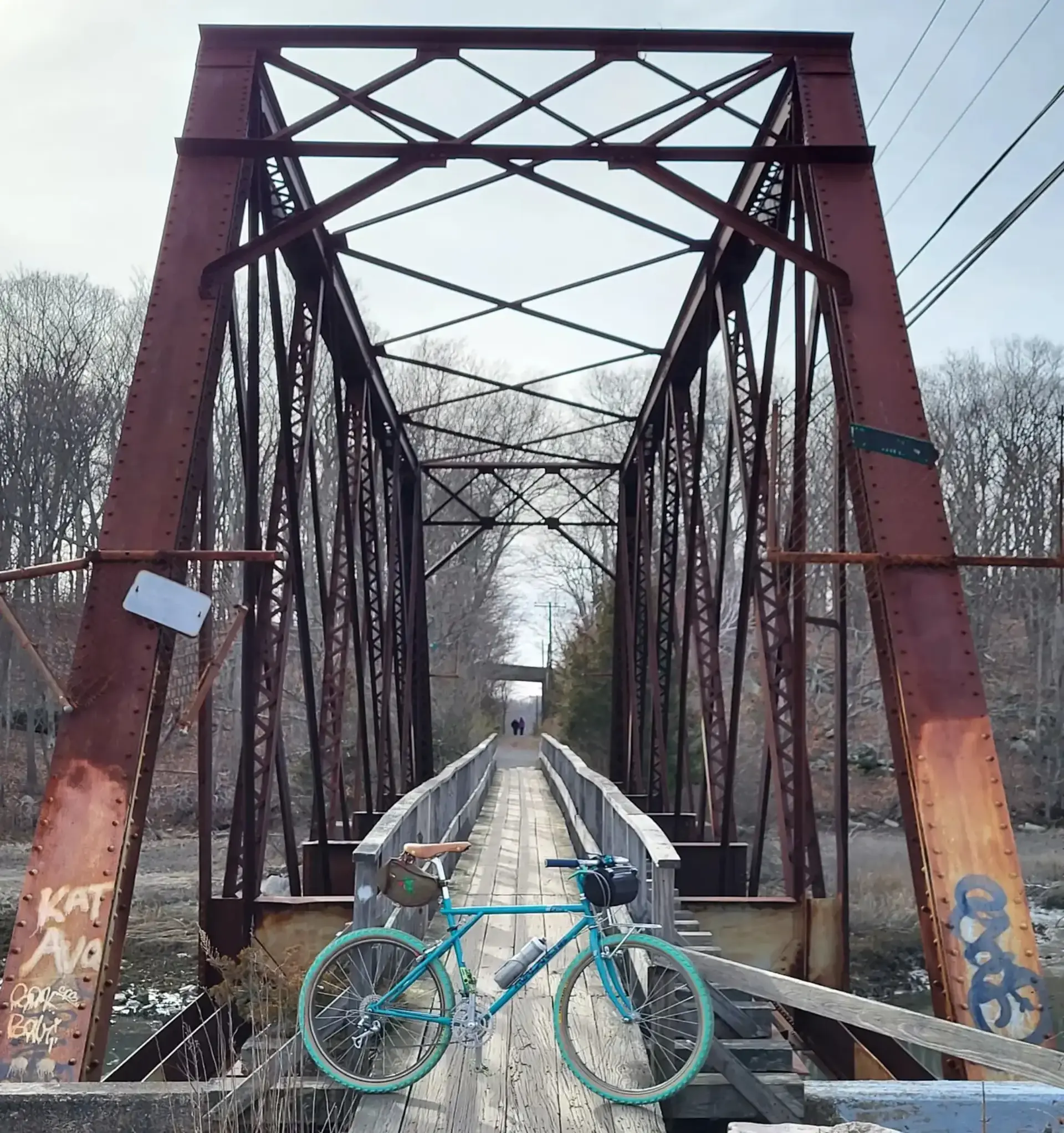 A turquoise bicycle on a rustic metal bridge under a bright sky.