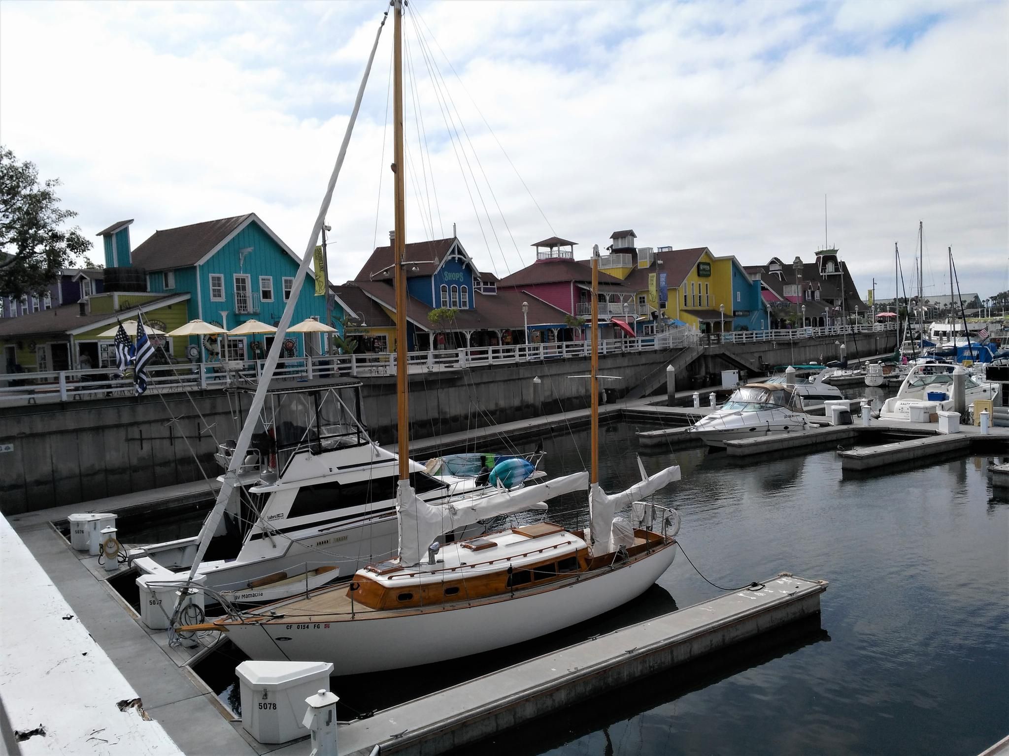 Boats docked in a marina with colorful buildings under an overcast sky. - Shoreline Beach Pedestrian Path