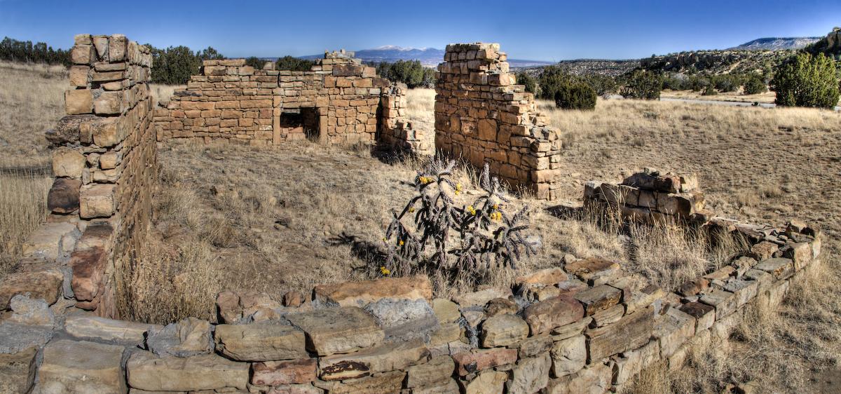 Ancient stone ruins stand in a dry, grassy field under a clear sky.