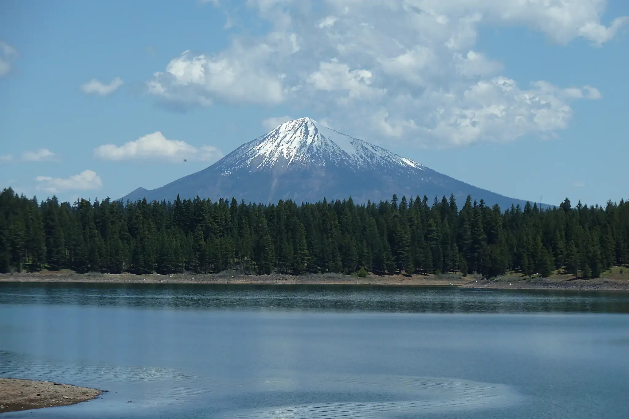 Snow-capped mountain rises above a lake and dense green forest.