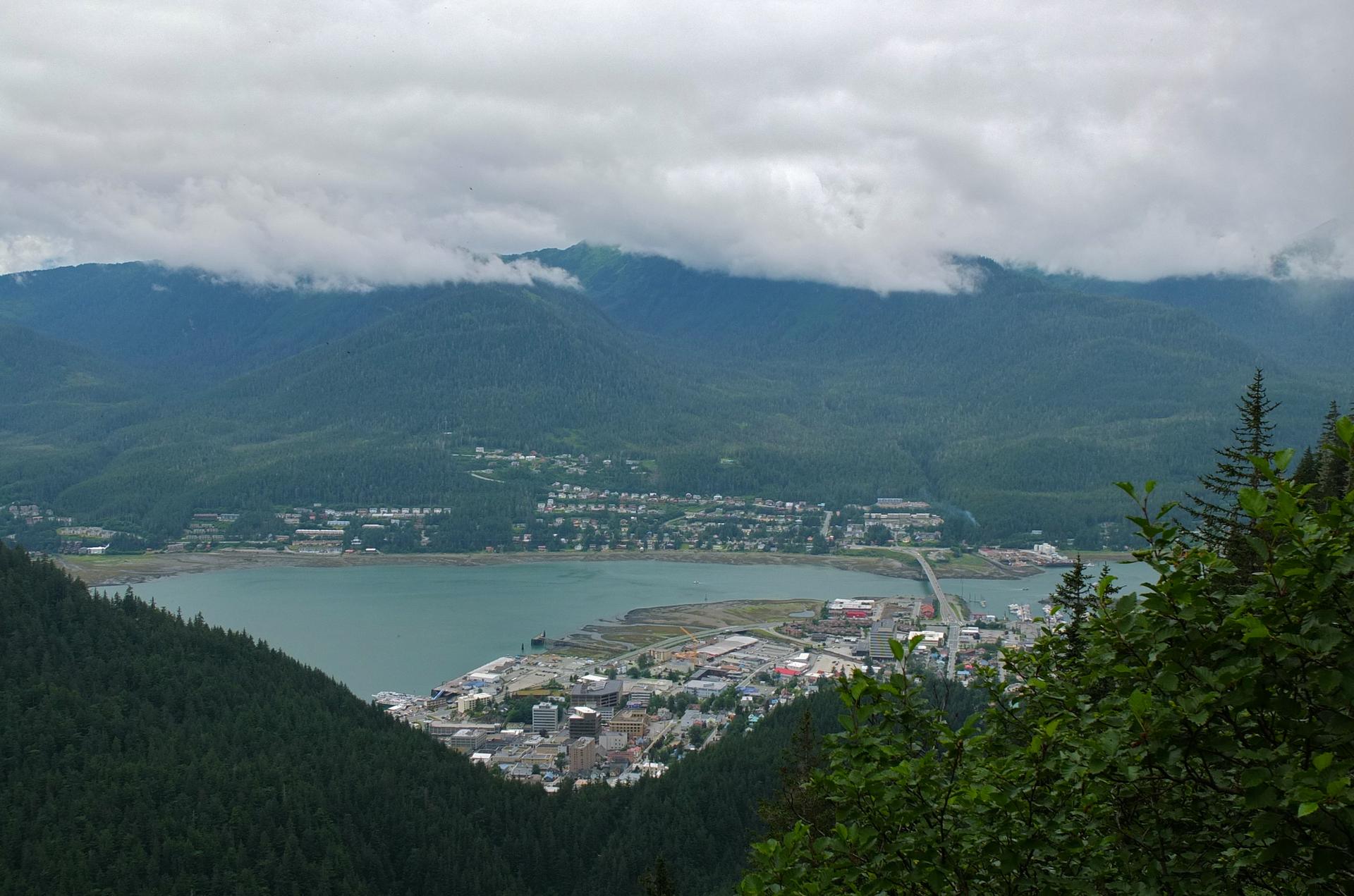 Aerial view of a coastal town and bay nestled among cloudy, forested mountains.