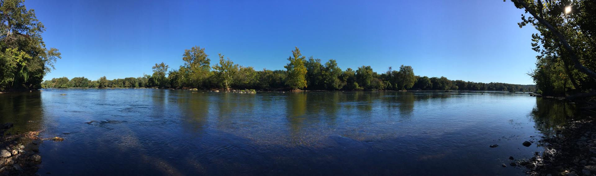 Panoramic view of a wide river with tree-lined banks under a clear sky.