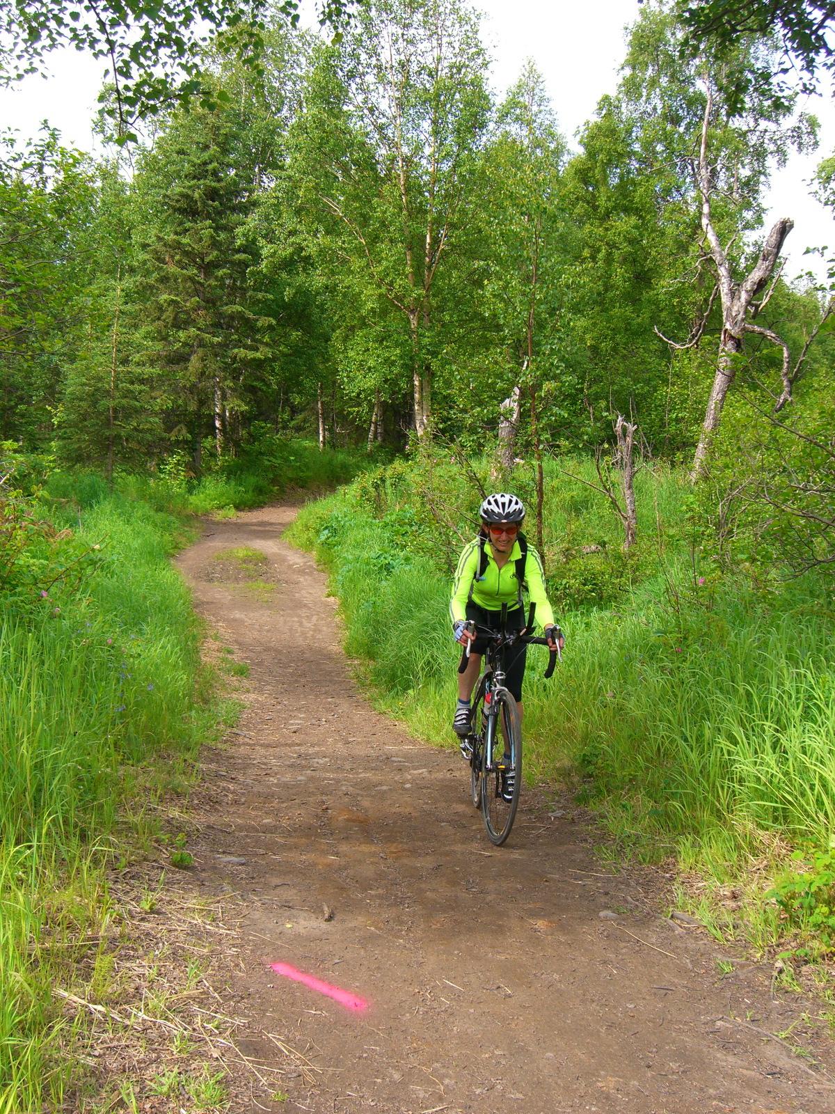 Person in bright green cycling on a dirt path through a green forest.