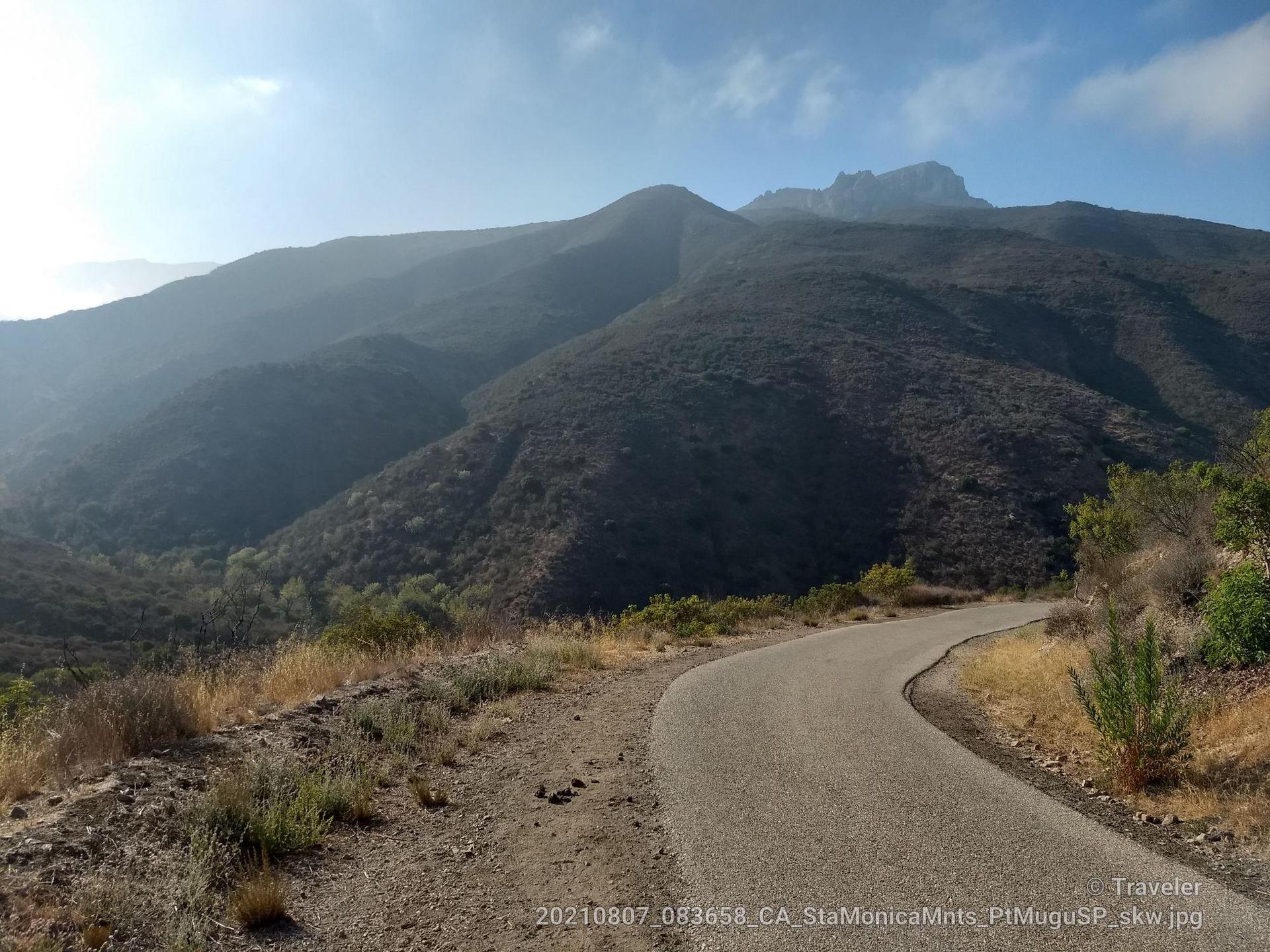 Paved road curves towards a large, dark mountain on a bright day.
