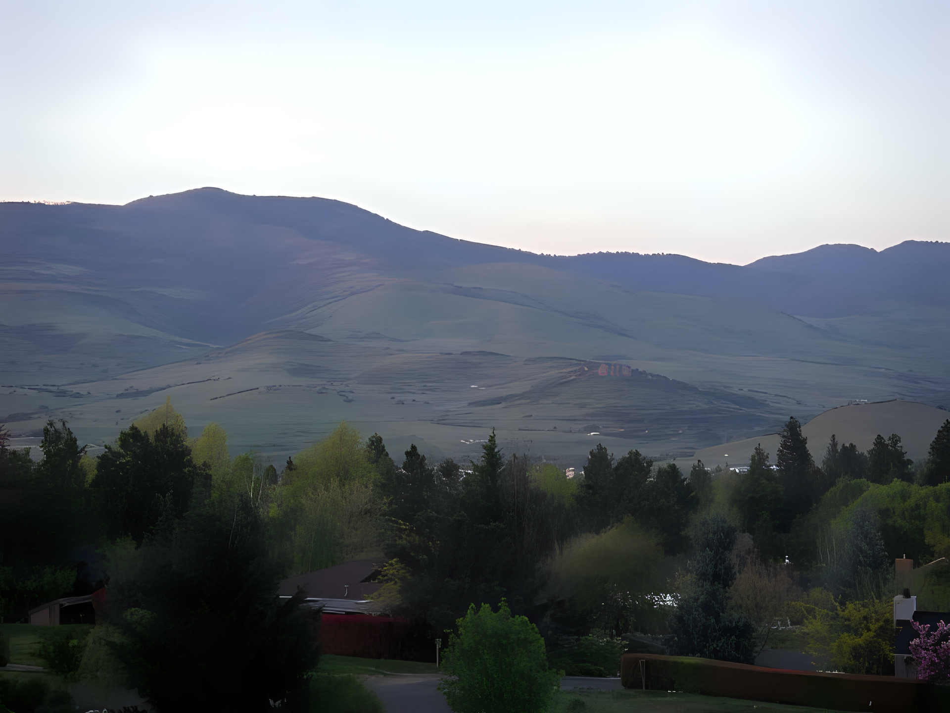 Distant mountains and a valley with trees and houses under soft, muted light.