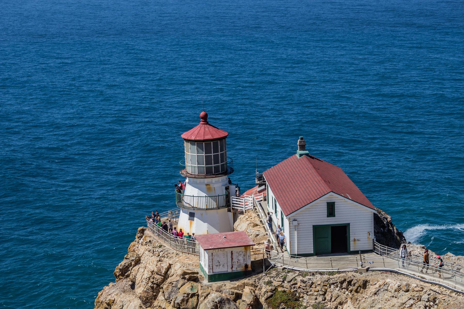 White lighthouse and building on a rocky cliff by the blue ocean.