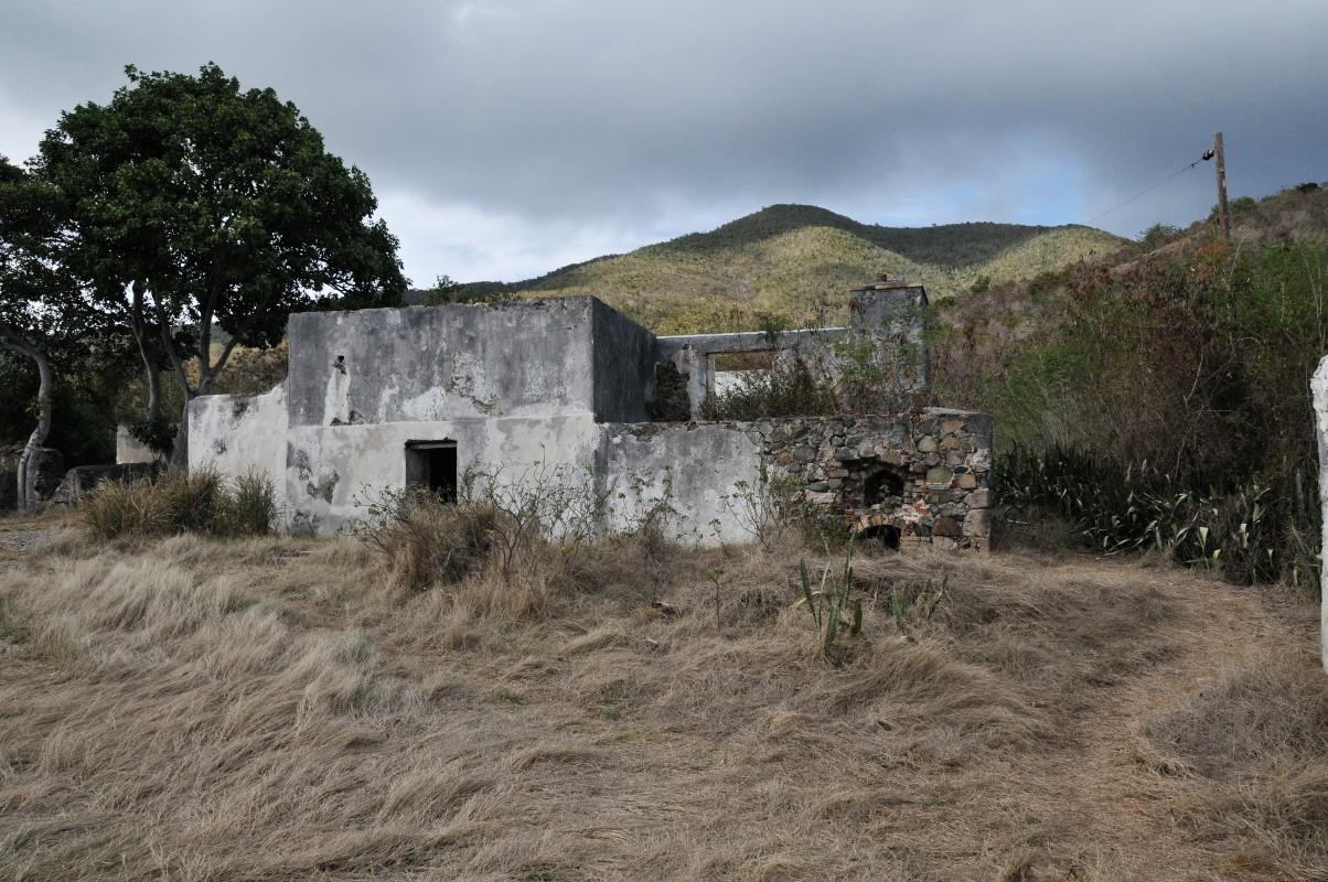 Weathered stone and concrete ruins on a grassy hill under a cloudy sky.