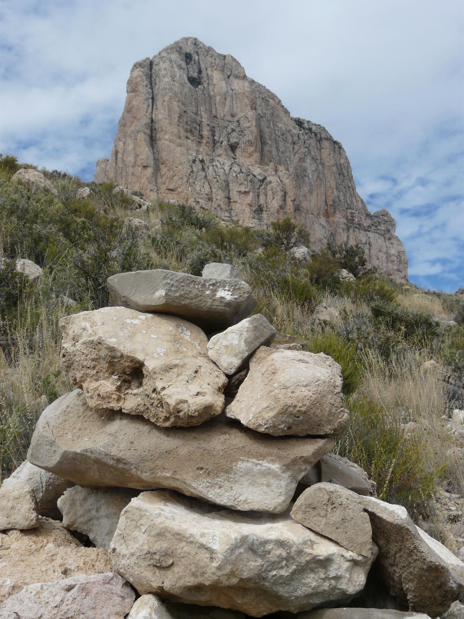 A cairn of stacked rocks in the foreground of a large rock formation.
