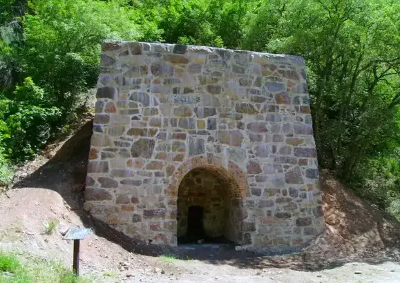Historic stone structure with an arched opening nestled in a green hillside.