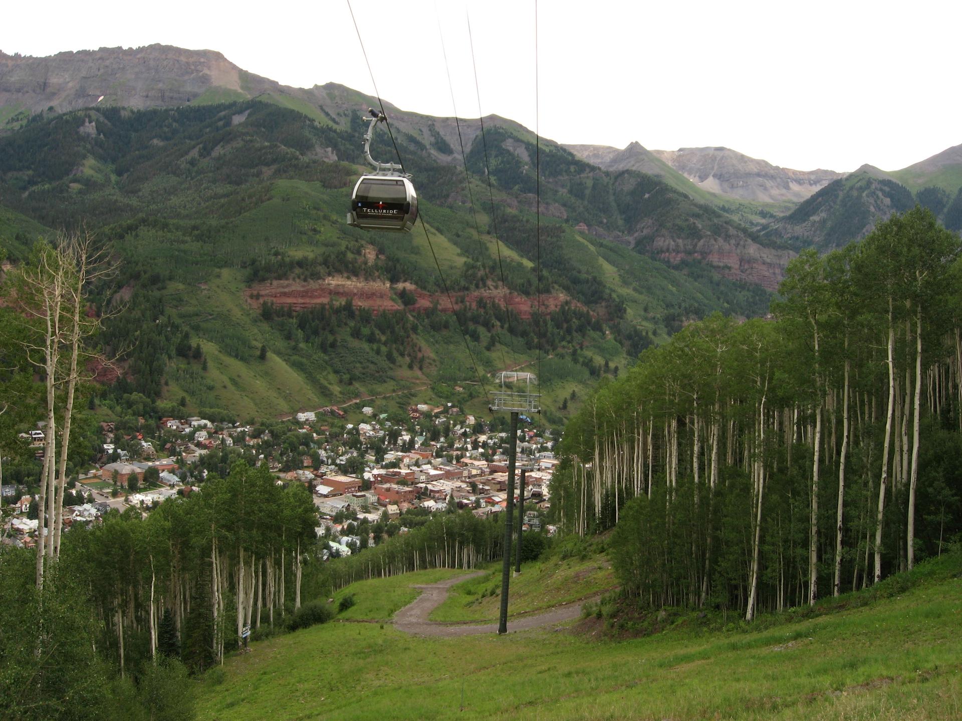 Gondola cabin over a mountain town with green slopes and aspen trees.