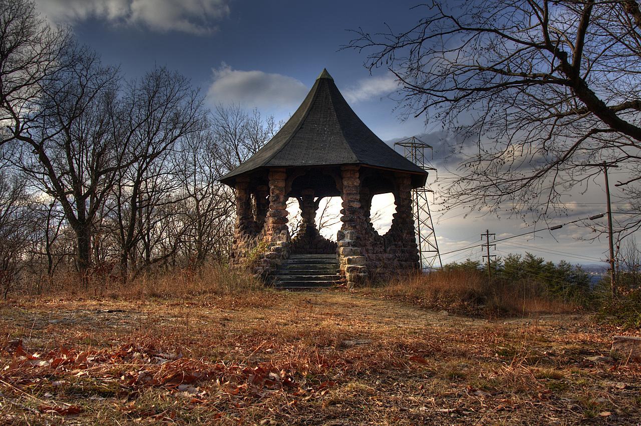 A stone gazebo on a hill, surrounded by bare trees and dry grass under a cloudy sky.