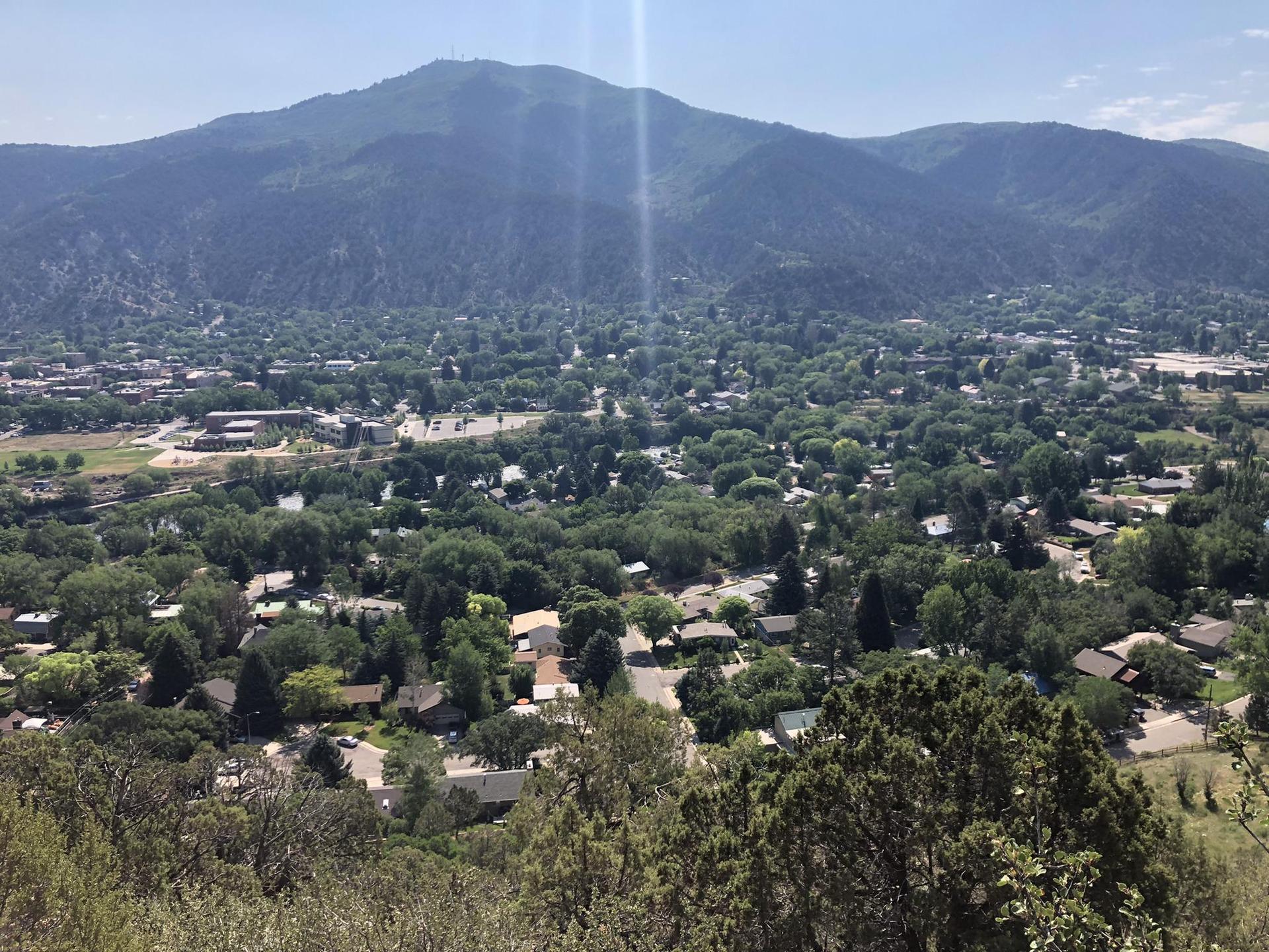 Sunny aerial view of a tree-filled town at the base of a large mountain.