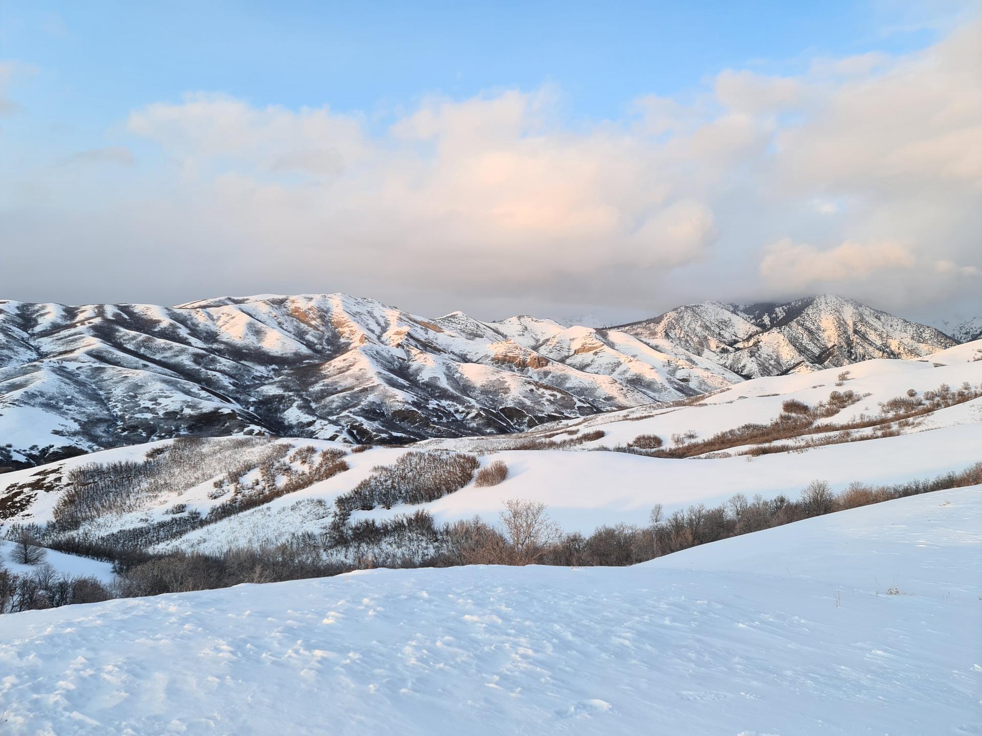 Snow-covered mountains and rolling hills under a partly cloudy sky at dawn.