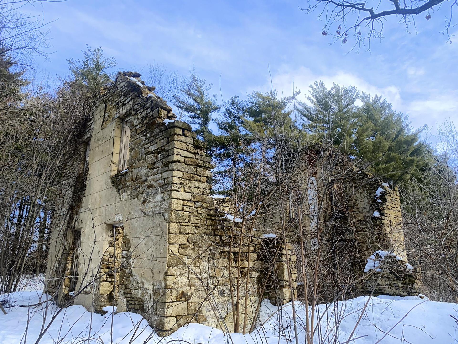 Ruined stone building covered in snow and bare branches under a blue sky.