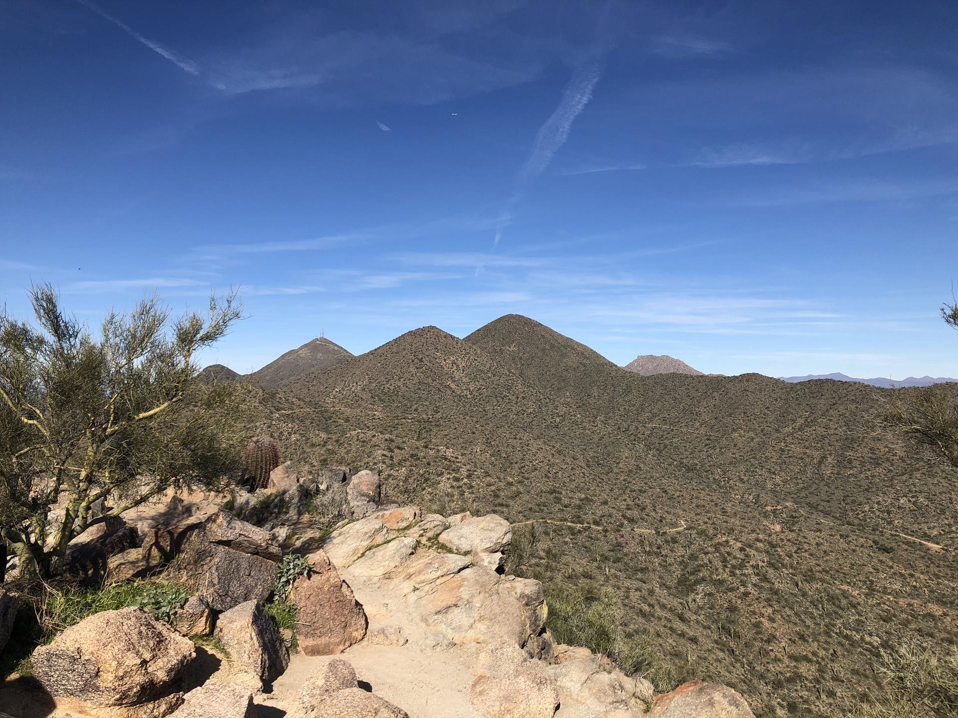 Sunny desert landscape with rocky foreground and distant arid mountains under a blue sky.