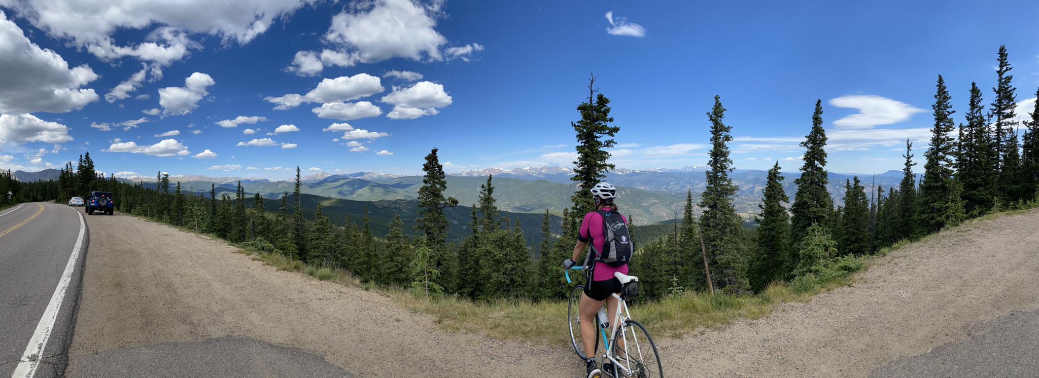 Cyclist admiring a vast mountain panorama under a bright blue sky.