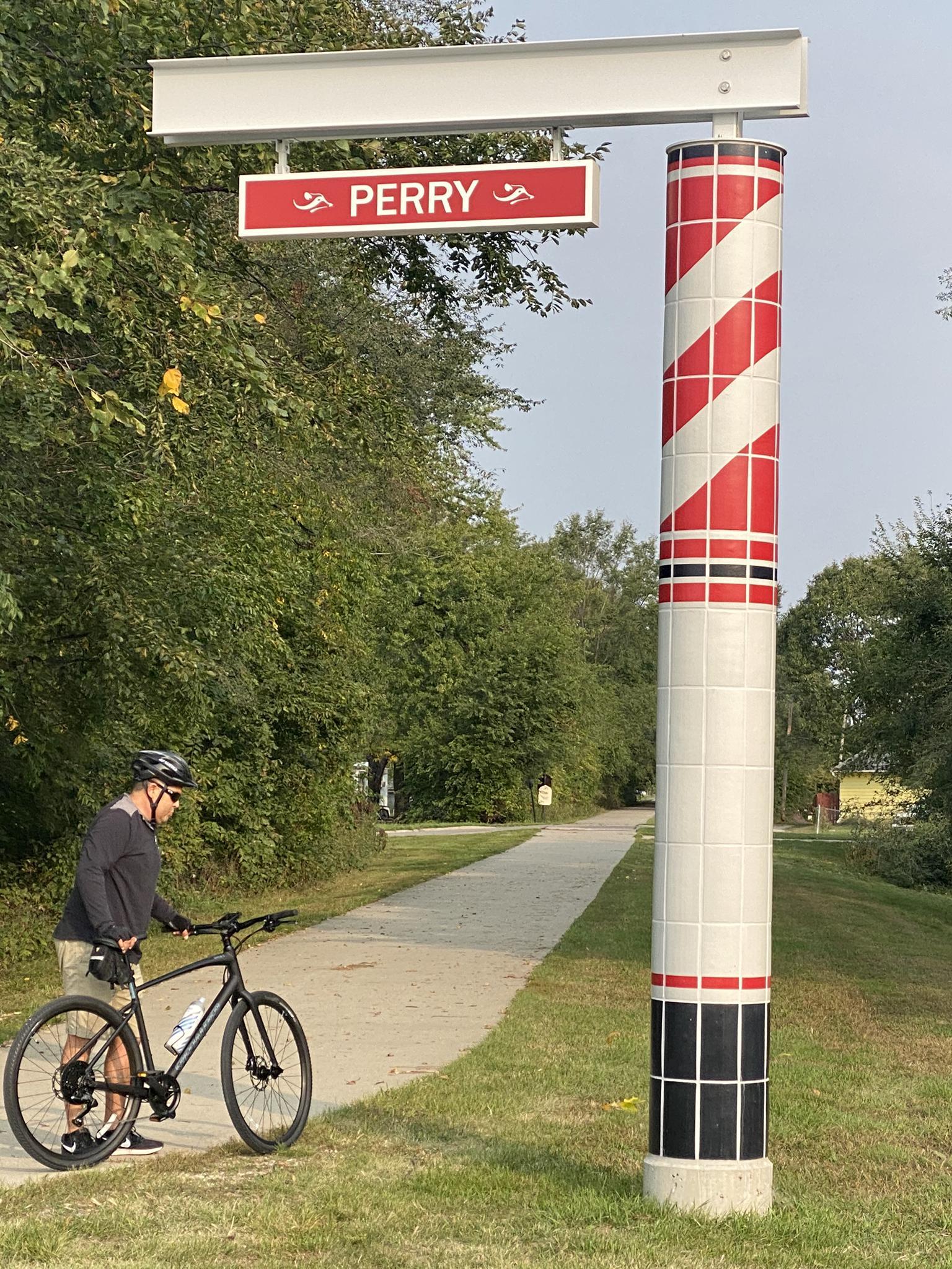 Cyclist standing next to a decorative pole and sign on a paved path.
