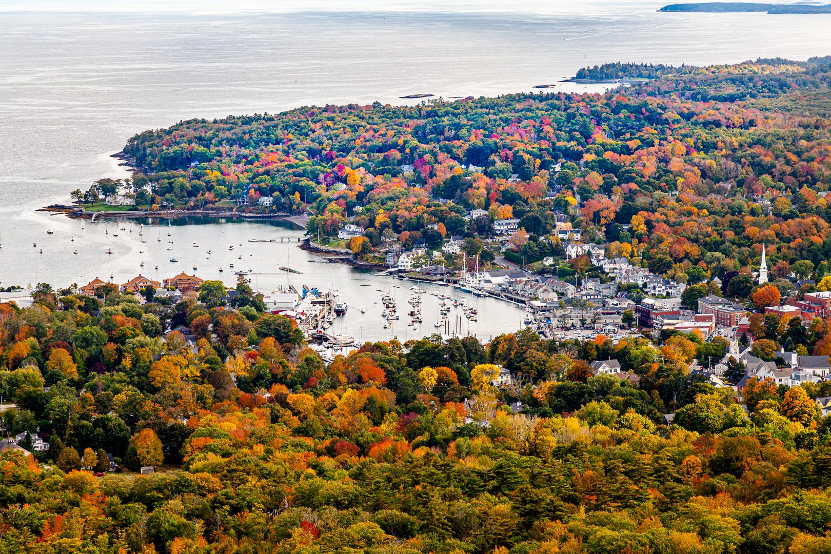 Aerial view of a coastal town and harbor surrounded by vibrant autumn foliage.