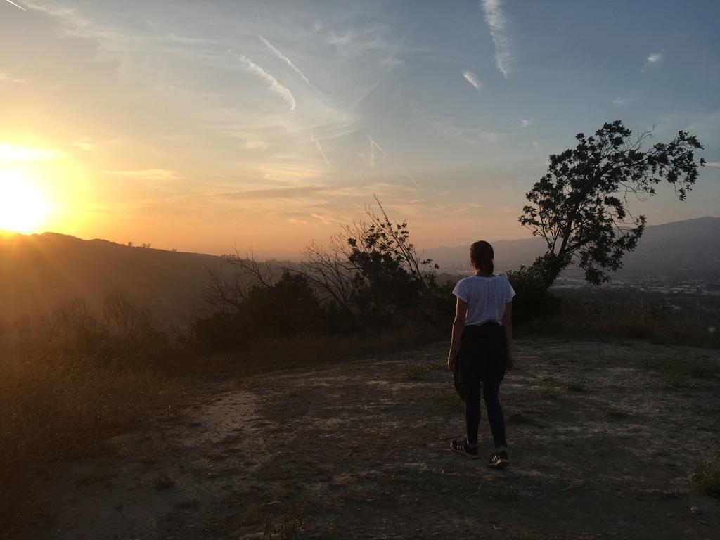 Person on hilltop watching a vibrant sunset over distant mountains.