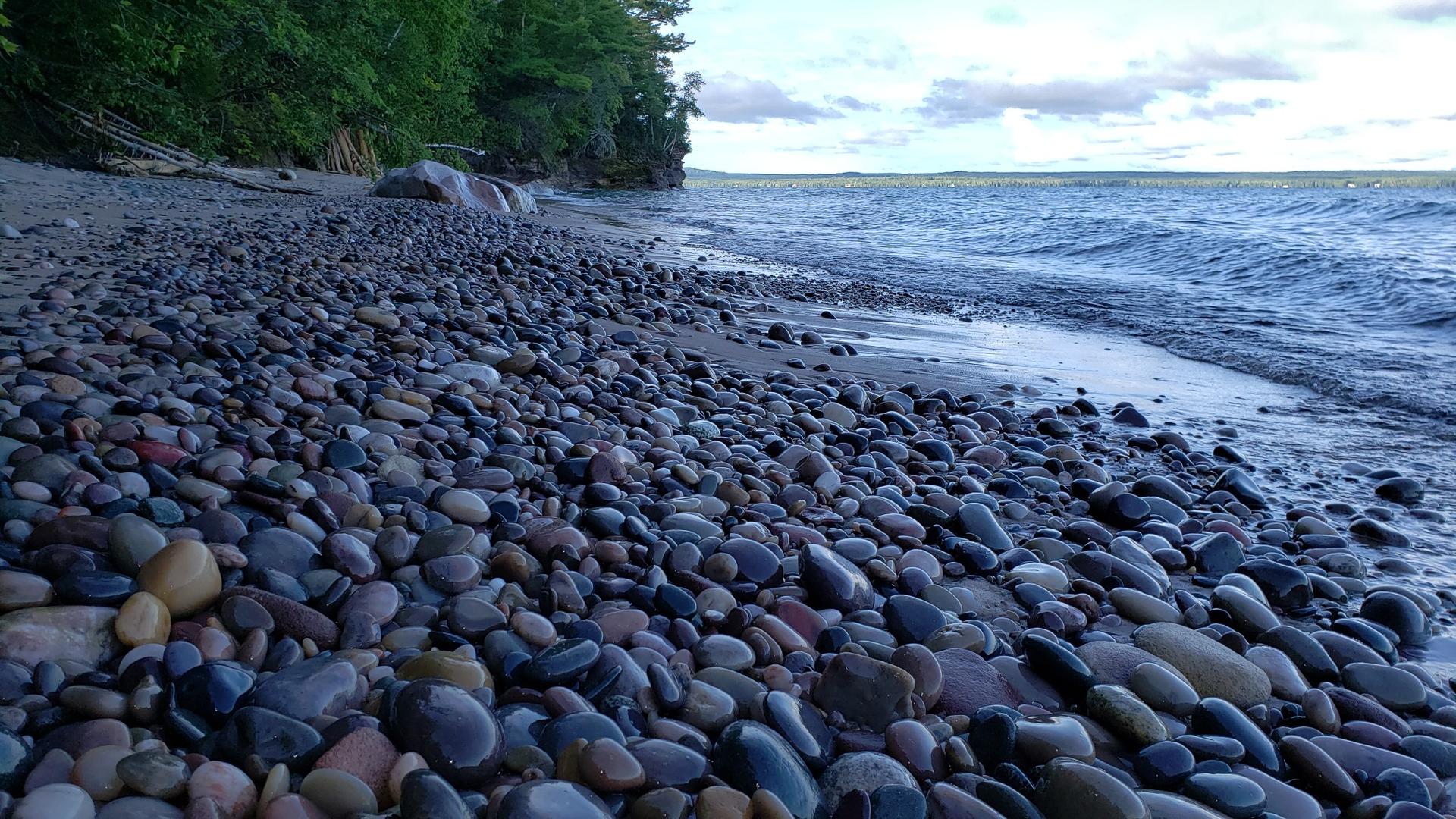 Pebble beach with waves under a cloudy sky.