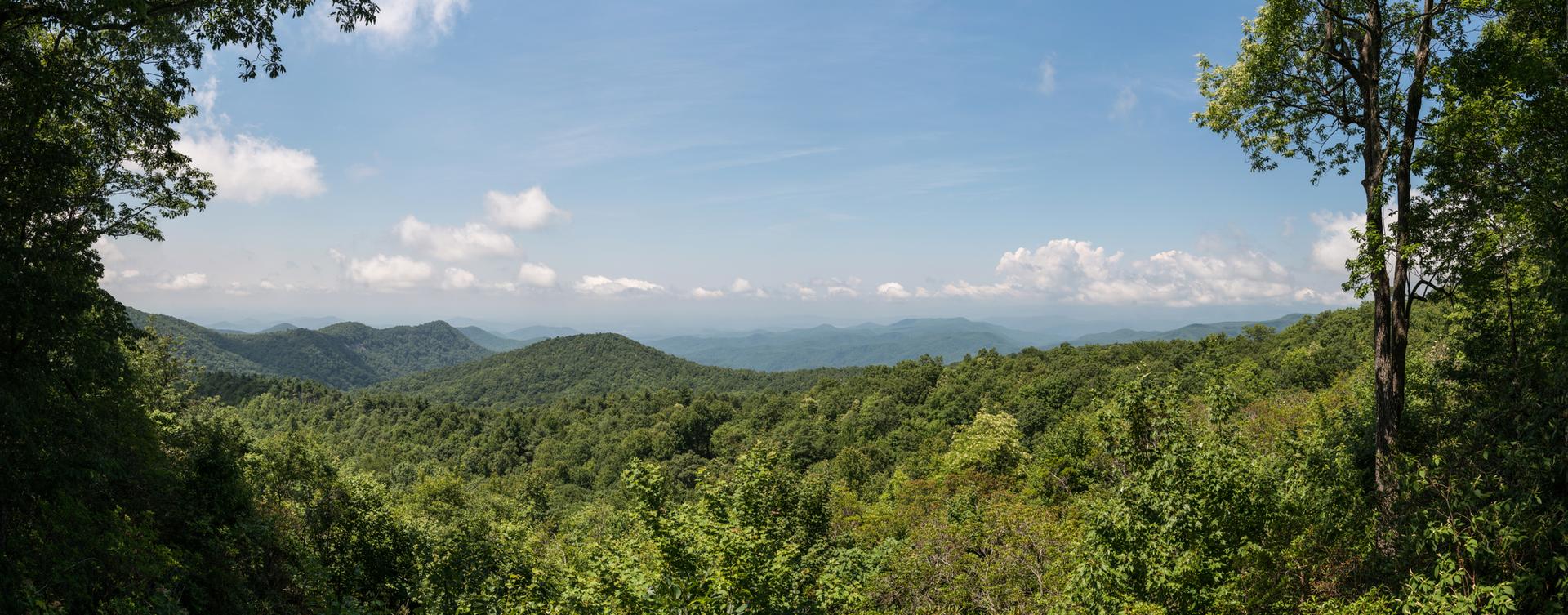 Panoramic view of lush green mountains under a bright blue sky with clouds.