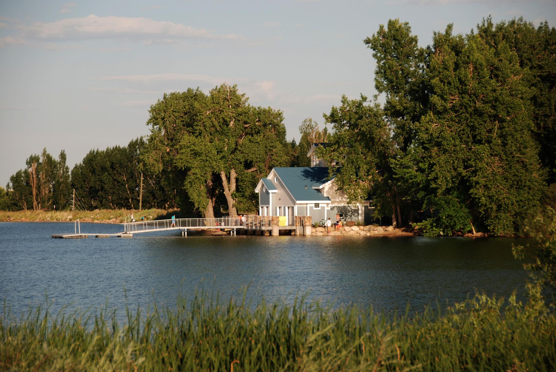 Lakeside house with a dock, surrounded by trees under warm light.