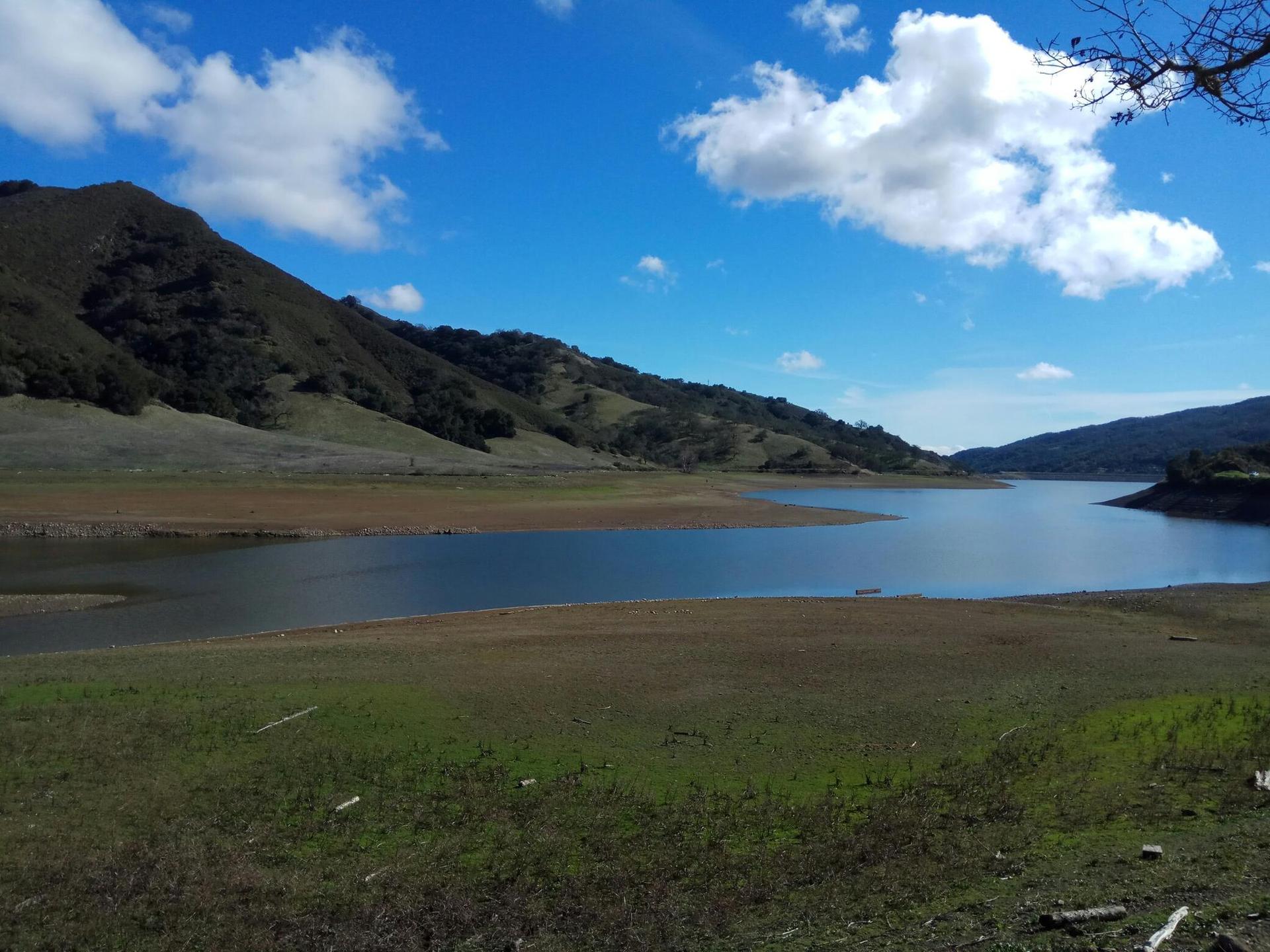 Expansive lake with exposed shoreline, surrounded by rolling hills under a bright sky.