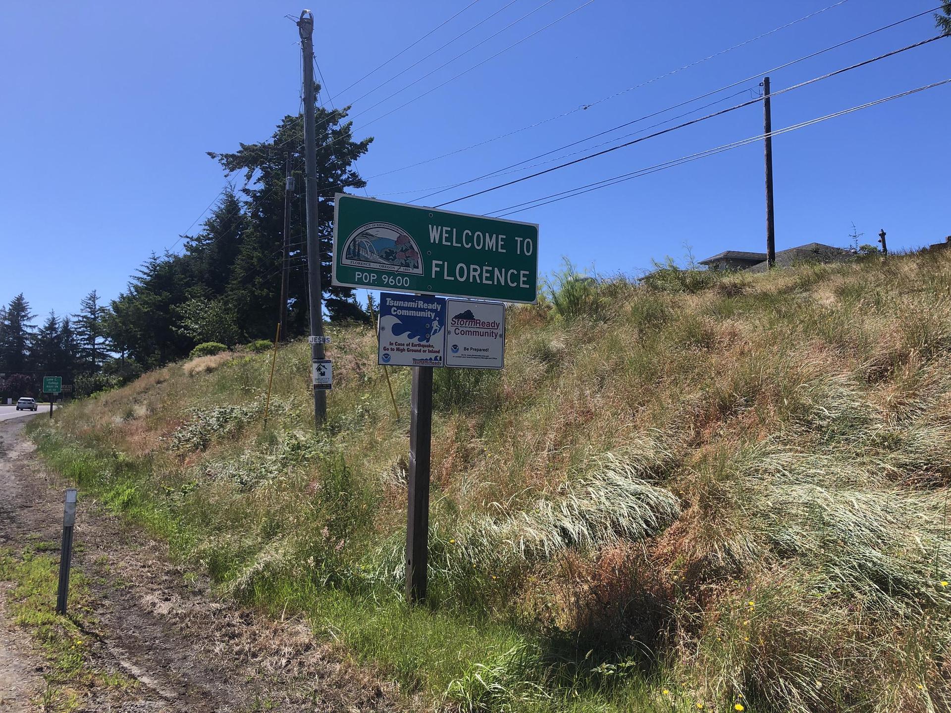 A green and white sign stands on a grassy hillside under a clear sky.
