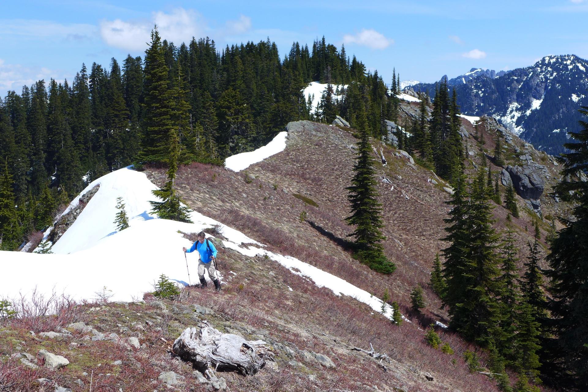 Hiker in blue jacket on a snowy mountain ridge under a bright sky.