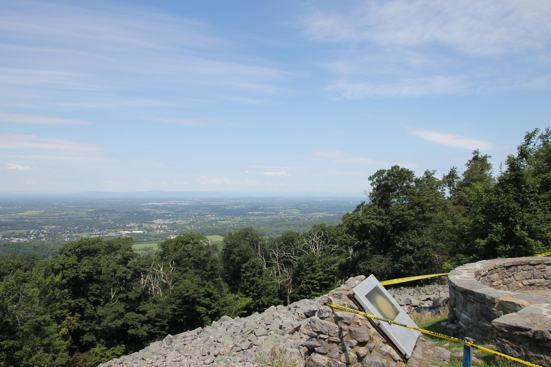 Sunny panoramic view of a vast green valley from a stone overlook.