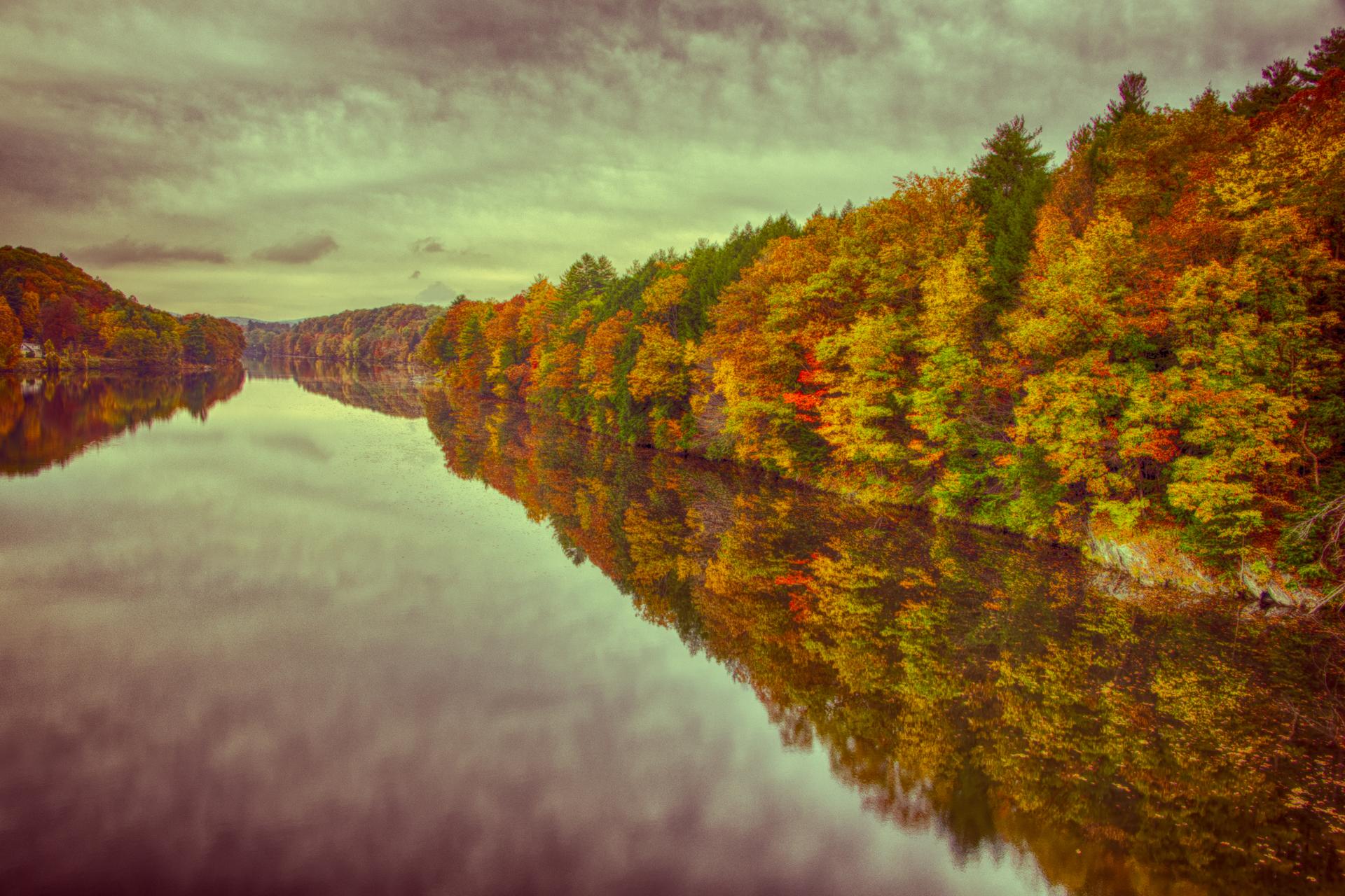 Overcast view of a river reflecting vibrant autumn trees on its banks.